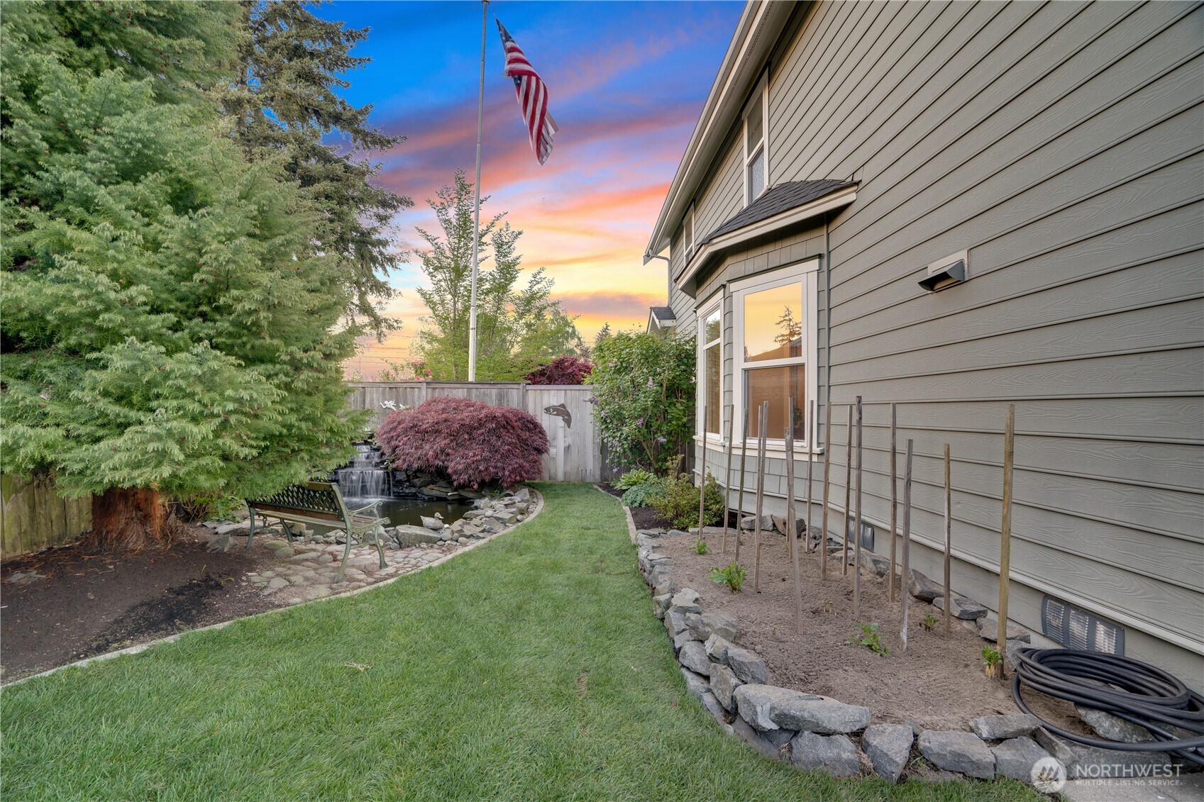 Back of the house at twilight. Primary balcony above. Waterfall in the background. The yard wraps around all of it.