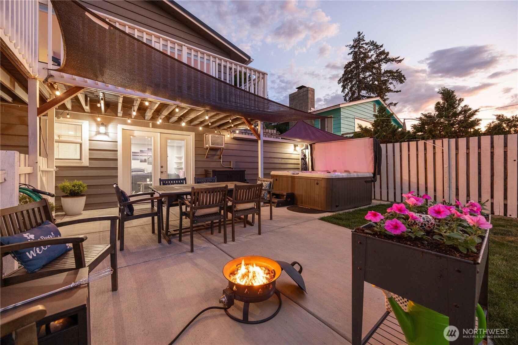 Twilight view of outdoor living space with dining area, private hot tub and fire pit.