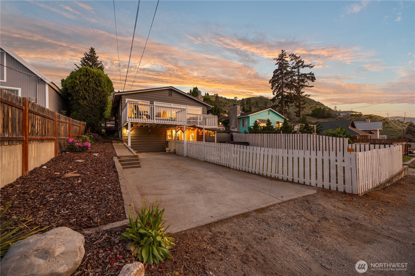 Exterior twilight view of home with landscaping, driveway and fenced yard.