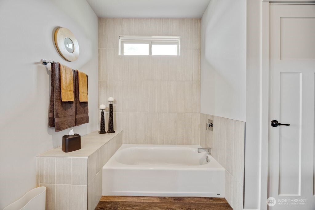 Spa-inspired primary bath featuring a low-profile tub designed for ease and comfort, paired with a walk-in shower and timeless tile finishes. Seller has retained matching tile, offering flexibility for future customization, including the option for a freestanding tub installation.