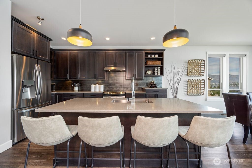 Spacious open-concept kitchen featuring a large center island, quartz countertops, under-cabinet lighting, and rich custom cabinetry with stylish display shelving