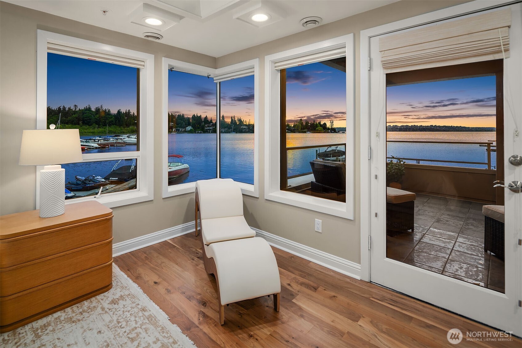 In the primary bedroom, corner windows wrap the sitting area in an unobstructed panorama of Lake Washington  while French doors lead directly to the expansive covered deck — seamlessly connecting the sanctuary within to the water beyond.