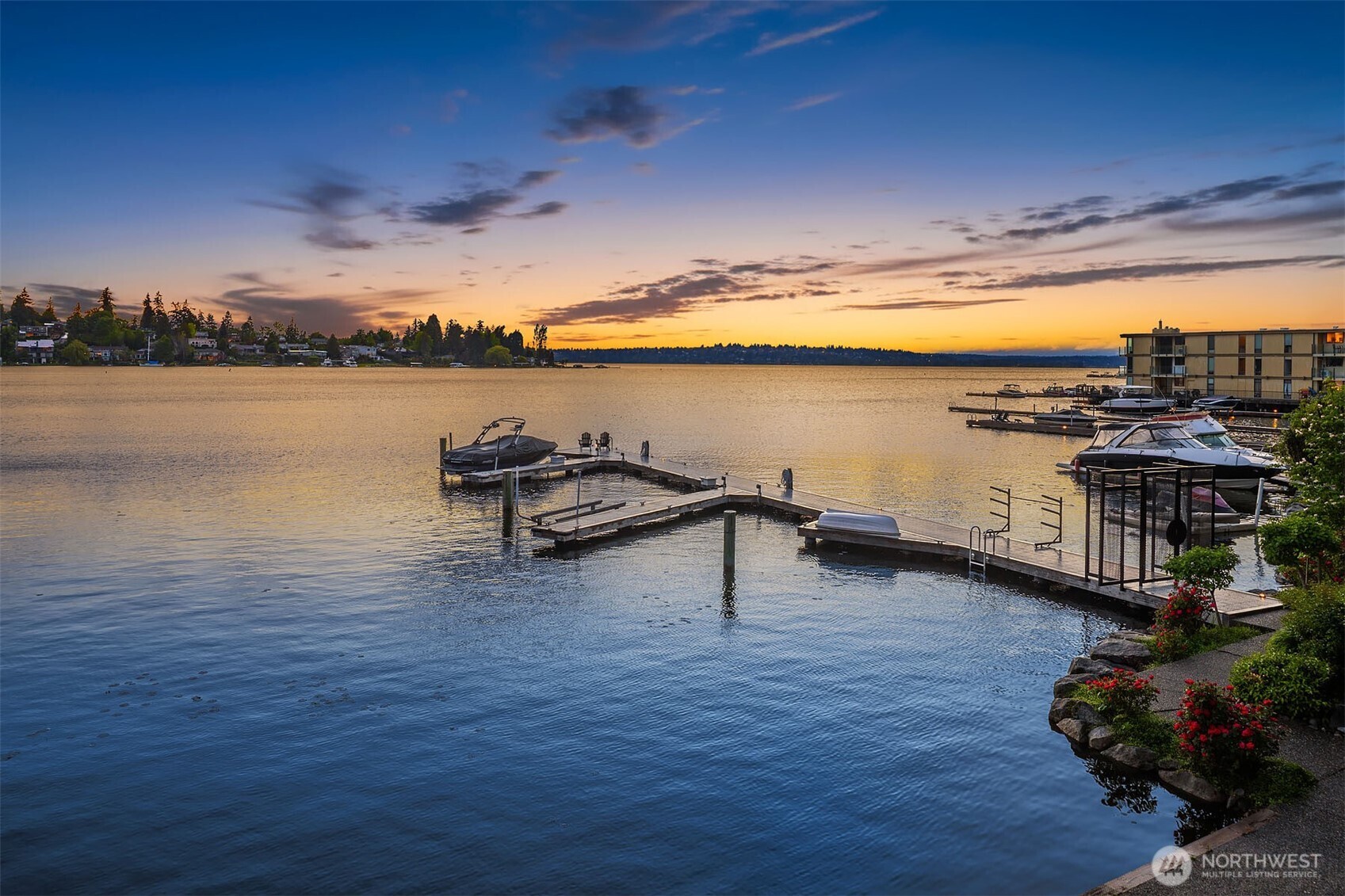 The full picture, reflected in the still waters of Yarrow Bay — a rare entire-floor residence in an exclusive four-home waterfront building, where lush grounds, multiple decks, and a private gated dock meet the practicality of an attached two-car garage with dedicated EV chargers and generous basement storage. A home that holds nothing back.