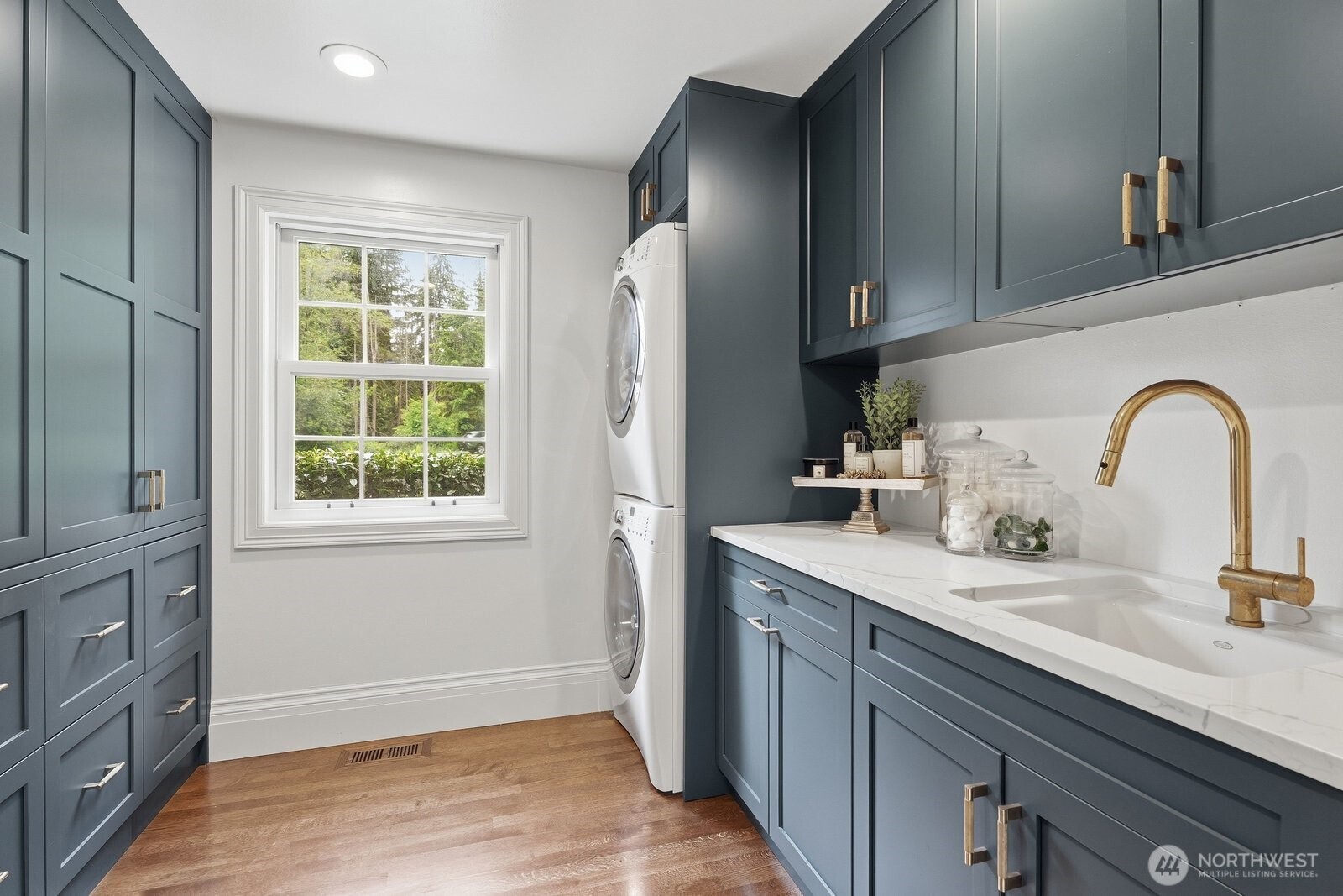 The large laundry room also outfitted with walls of custom cabinets, built-in laundry sorting bins, utility sink and quartz counter.