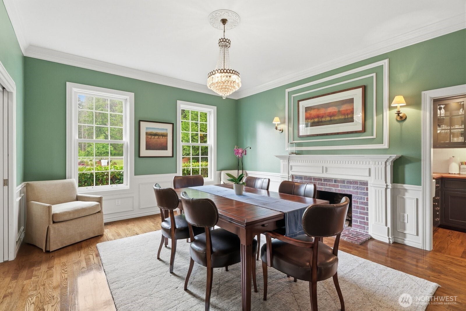 The formal dining room with wainscoting, crown molding also with a brick surround wood burning fireplace and crystal chandelier.