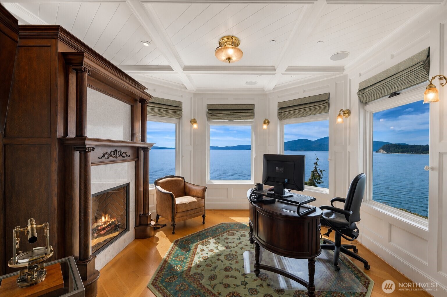 The private home office within the primary suite offers an inspiring workspace with custom built-ins, cozy seating, and panoramic water views.