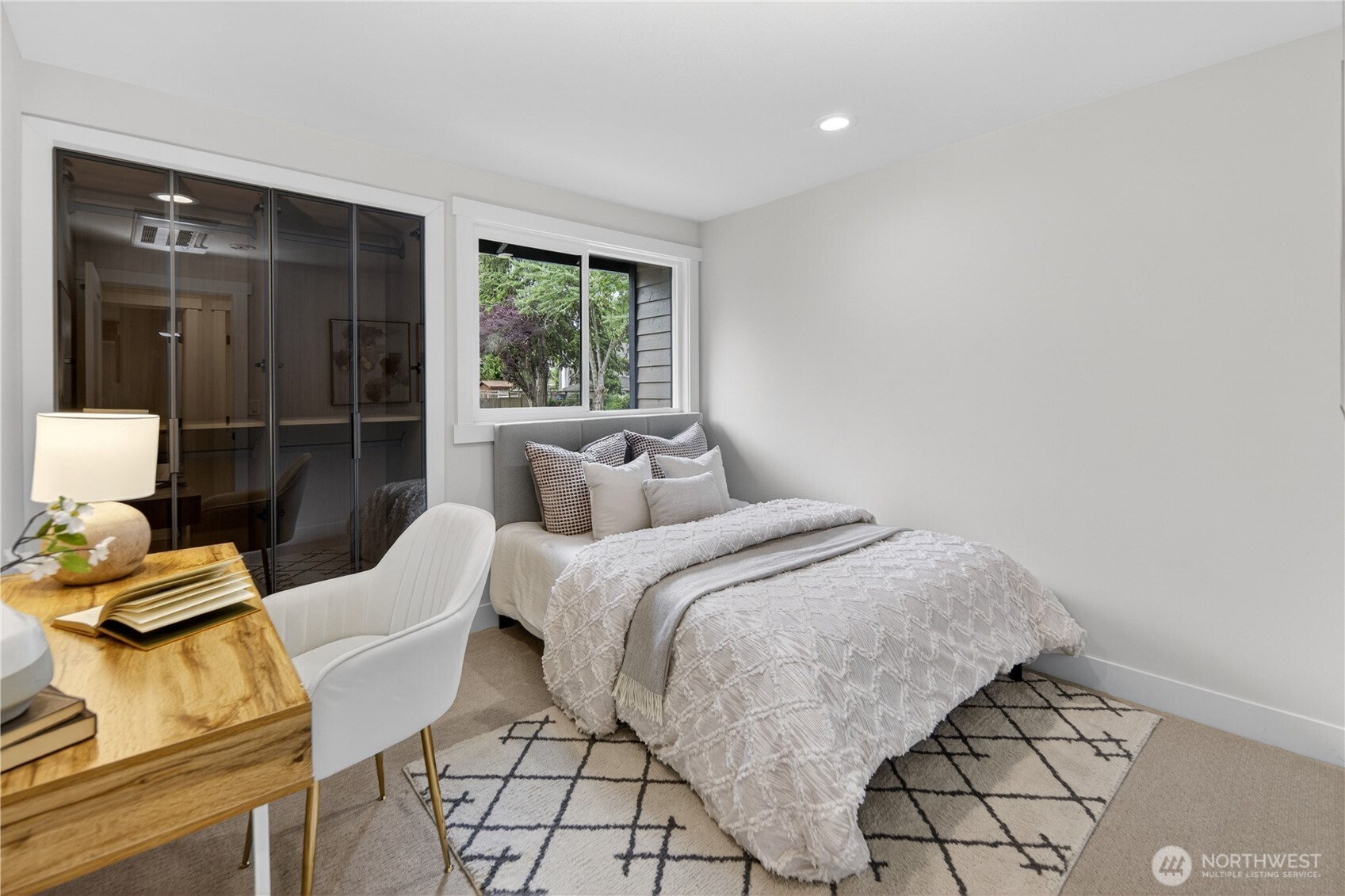 The first bedroom on the right side of the hallway feels soft and restful with new carpet underfoot, a gently slanted ceiling, and a new flush-mount ceiling light paired with recessed lighting for a warm, even glow. Modern smoked-glass closet doors with slim black framing add a stylish designer touch, opening to a generous closet for excellent storage.