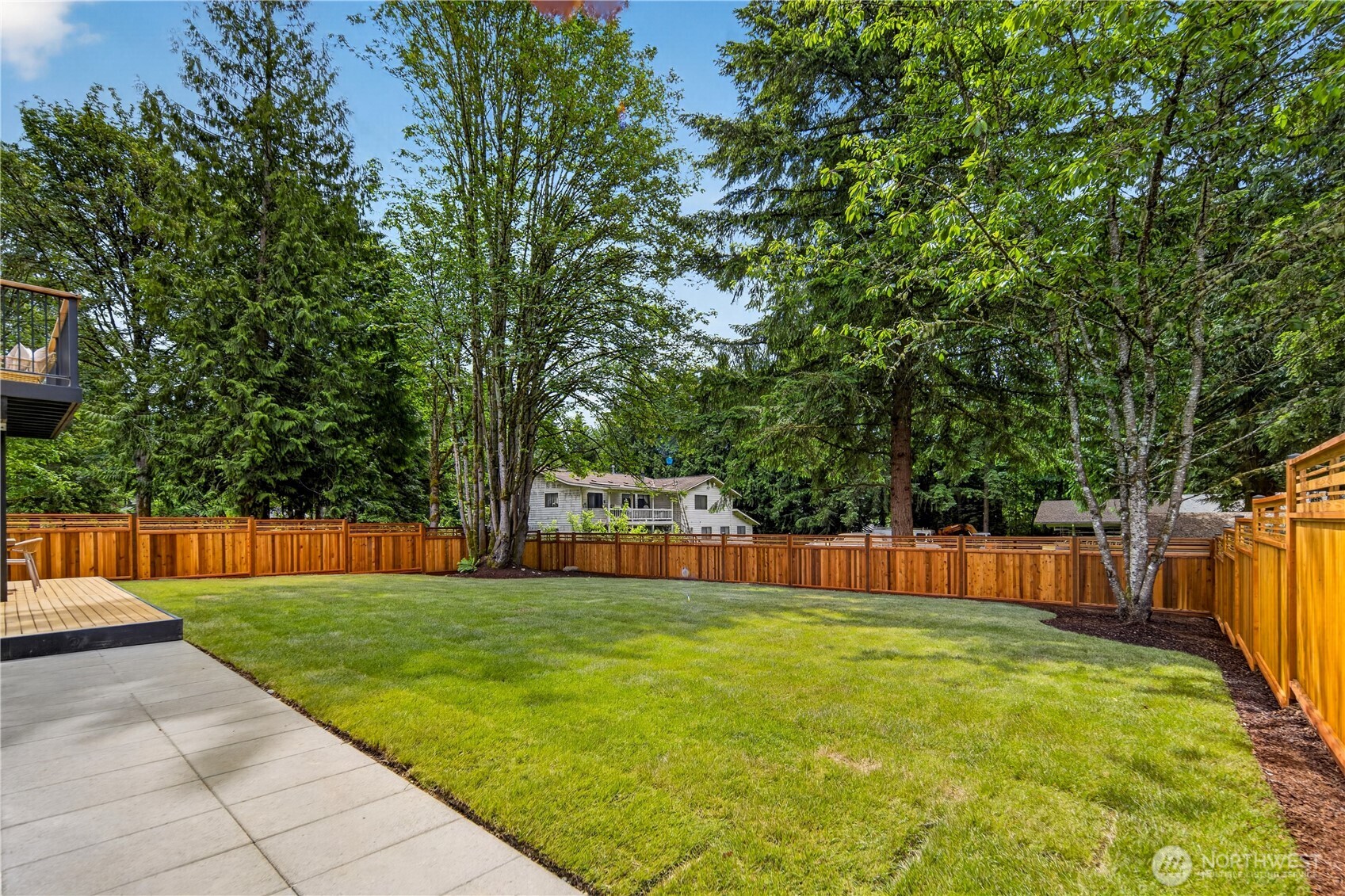 Beyond the deck, a large patio extends the outdoor living space and creates room for even more enjoyment of the back yard. It is easy to imagine lounge seating, play space, container gardens, or even a hot tub here, all alongside the flat lawn and lovely trees. Together, the deck, patio, and yard create a spacious setting for relaxing, entertaining, and everyday outdoor living.