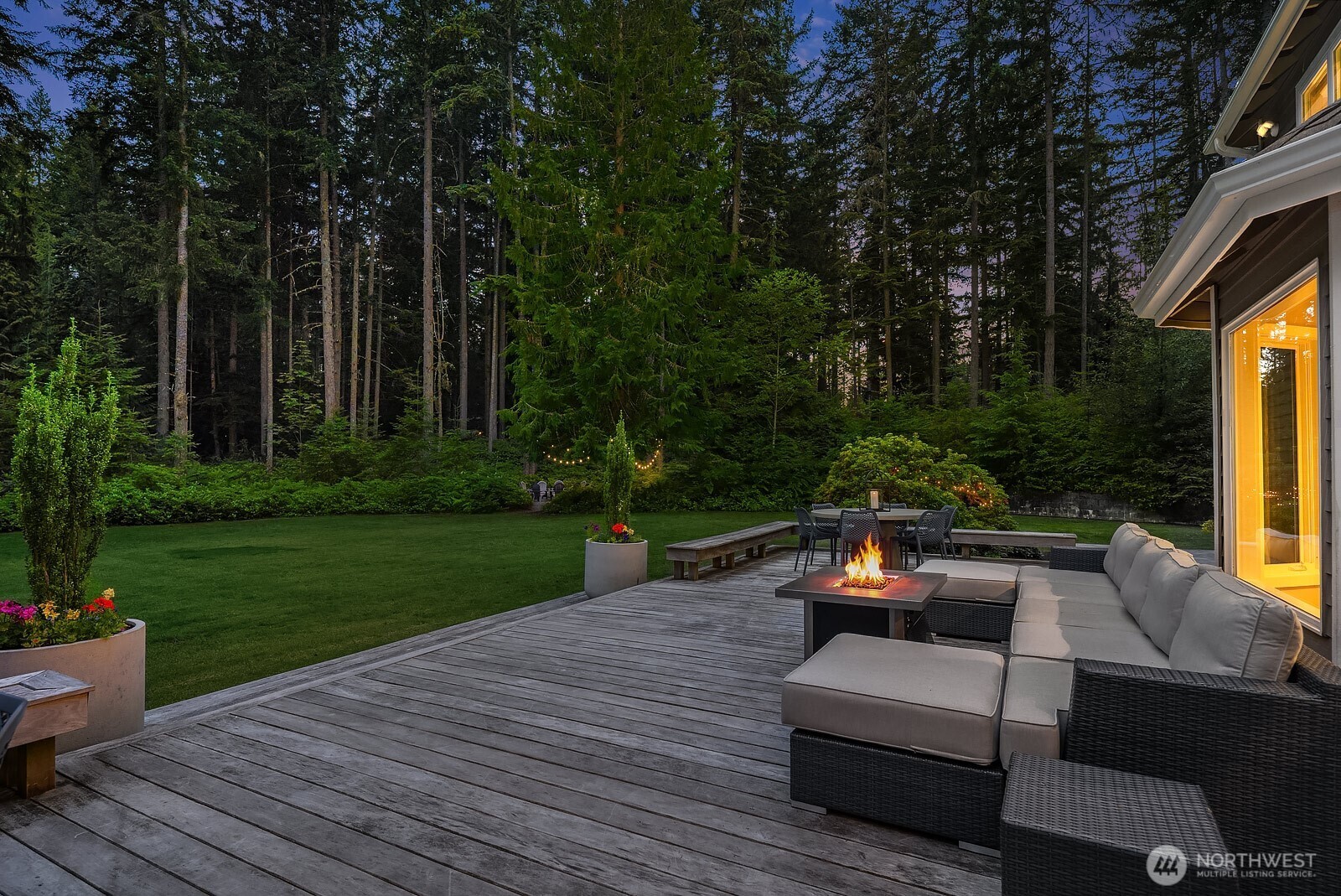 The stunning Garapa hardwood deck is the perfect backdrop for evening entertaining, featuring a cozy fire pit seating area surrounded by lush, mature evergreens for complete privacy.
