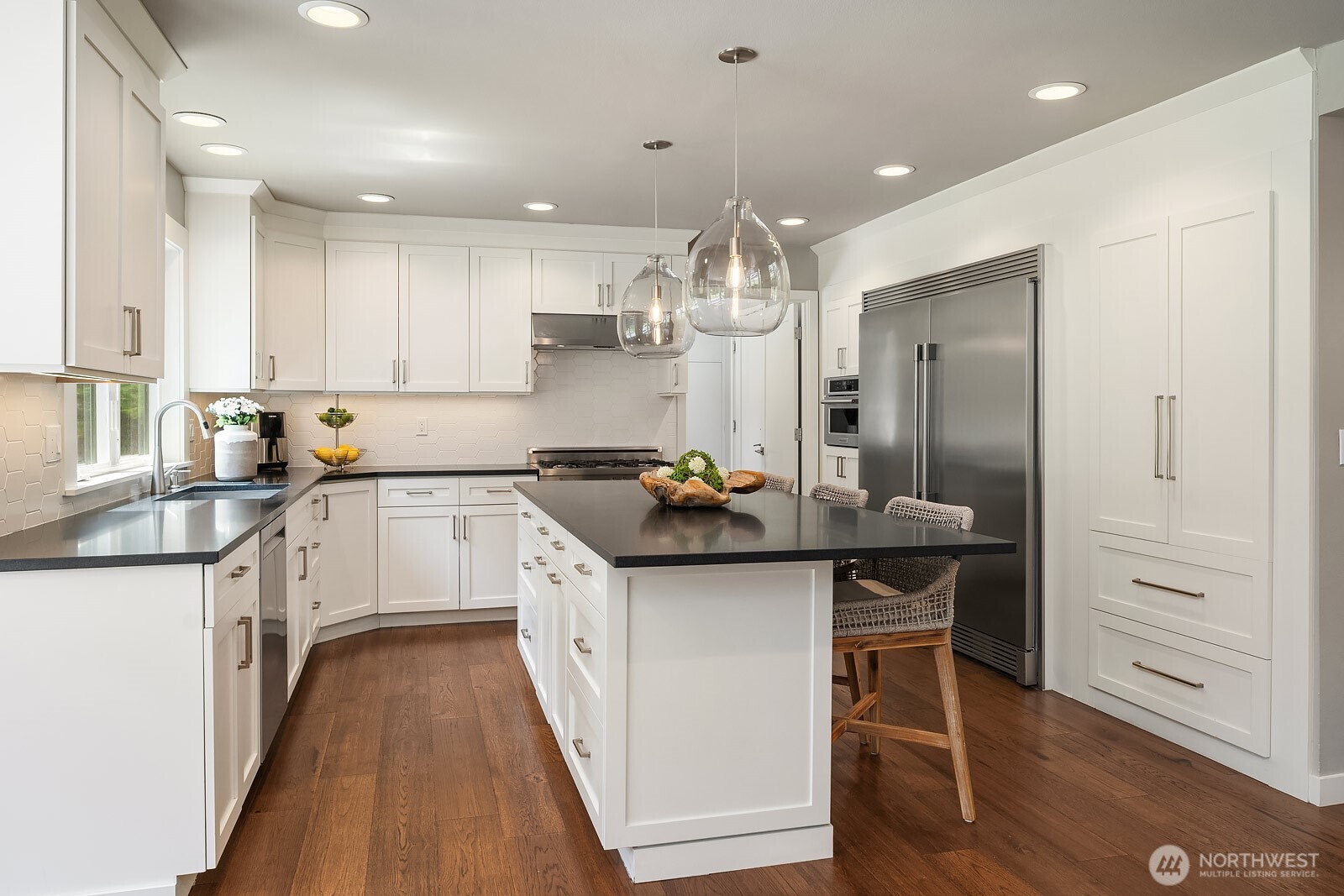 The chef's kitchen showcases crisp white cabinetry, dark stone countertops, stainless steel appliances, and designer lighting, delivering a stylish and highly functional space at the heart of the home.