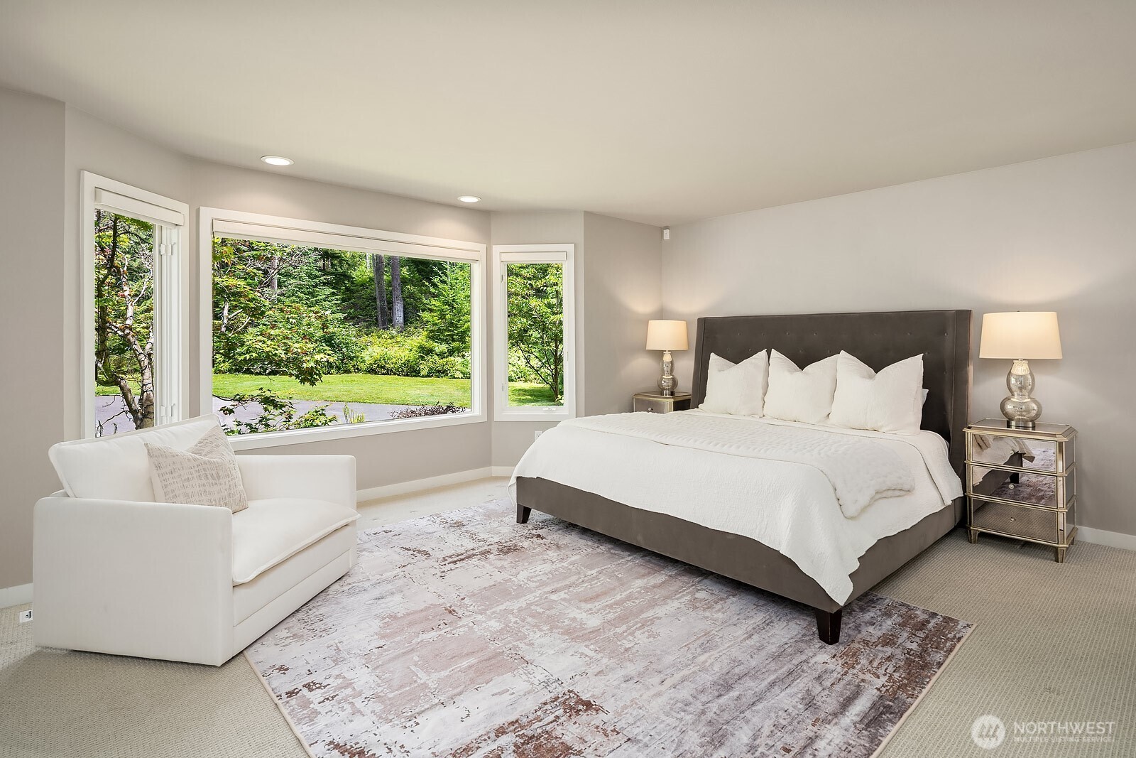 The main-level primary suite is a serene retreat, bathed in natural light from large windows framing lush garden views, with generous space for a sitting area and a peaceful, private atmosphere.
