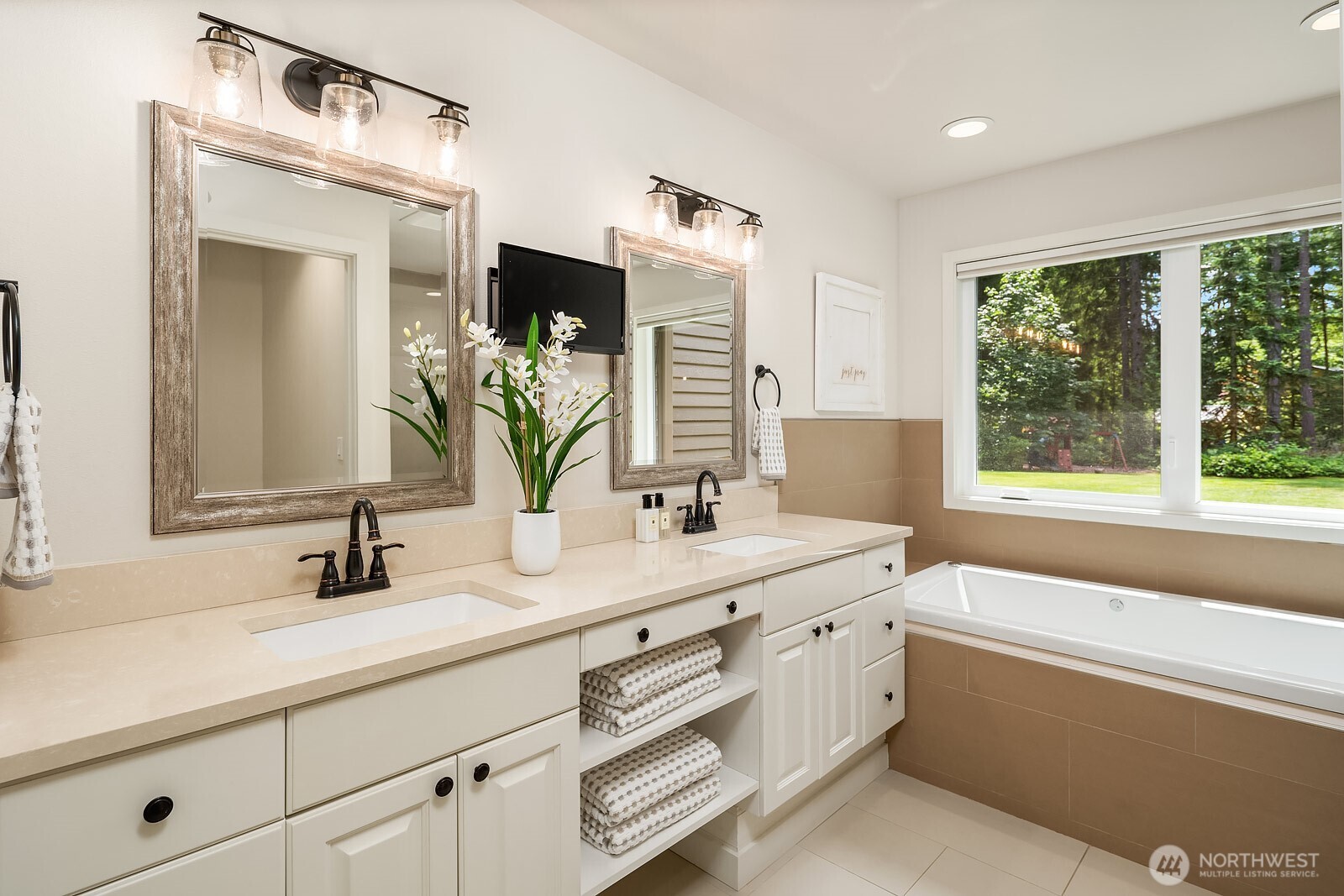 The primary bath features a dual vanity with updated finishes, a soaking tub beneath a bright window, and a clean, spa-like aesthetic that completes the main-level primary suite.