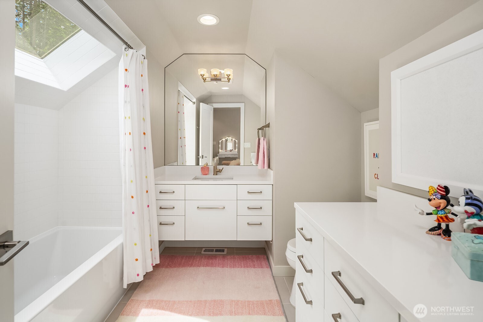 This spacious bathroom features dual vanities, a soaking tub, and a skylight that fills the space with natural light, offering a bright and functional retreat for the upstairs bedrooms.