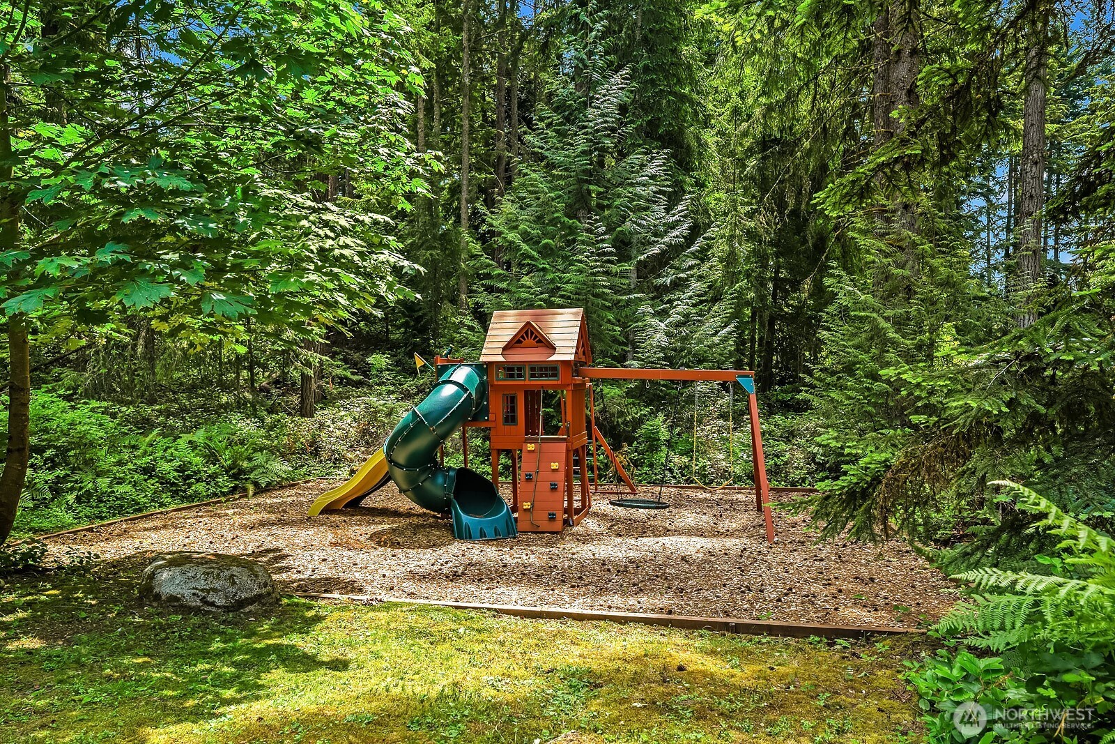 The playset is nestled among the trees in its own dedicated area, offering a fun and naturally shaded space for kids to play within the privacy of the fully fenced 2.22-acre property.
