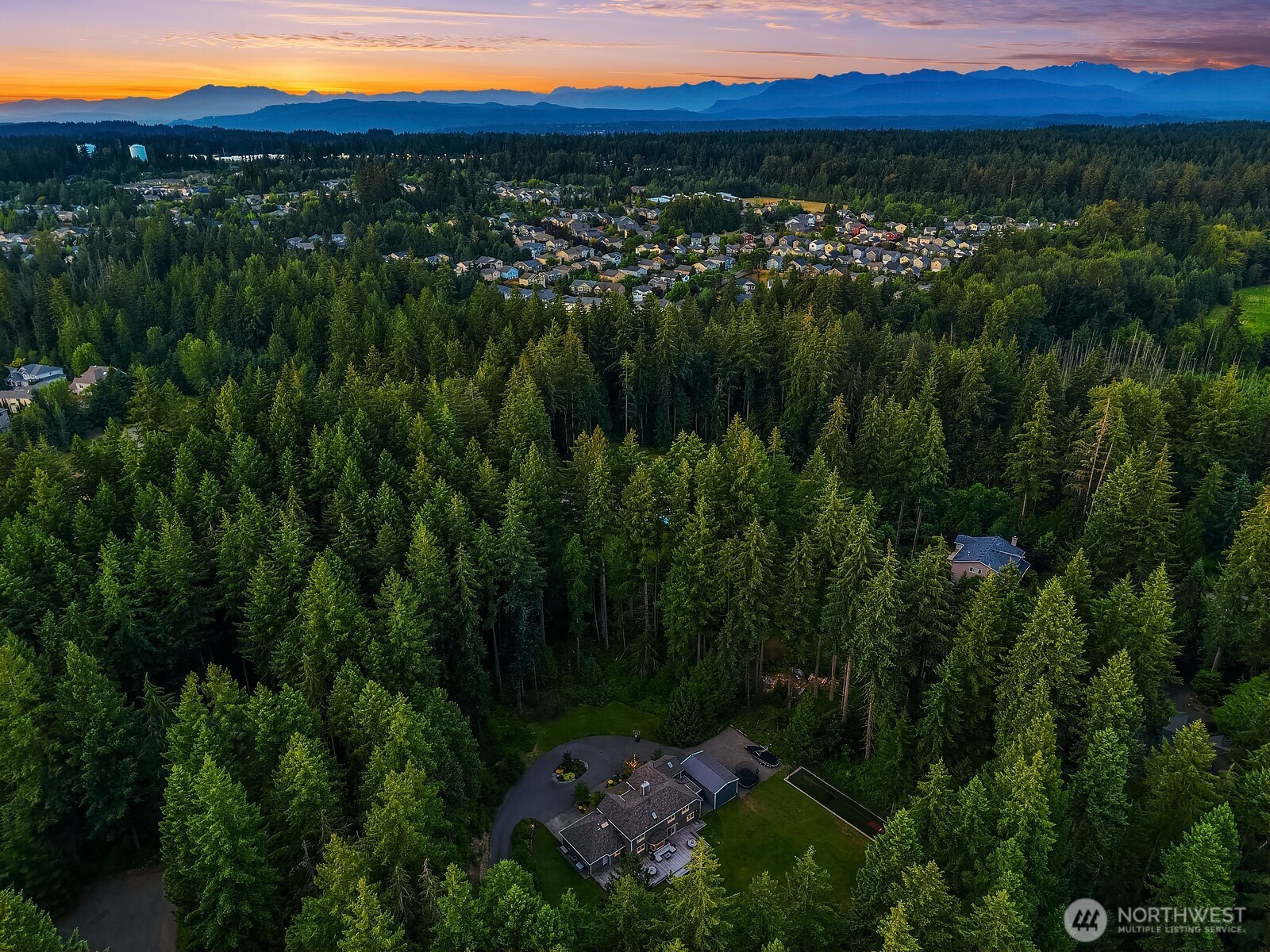 A sweeping aerial view at sunset showcases the property's prime Union Hill location, surrounded by lush Pacific Northwest forest yet conveniently close to the community and amenities beyond the tree line.