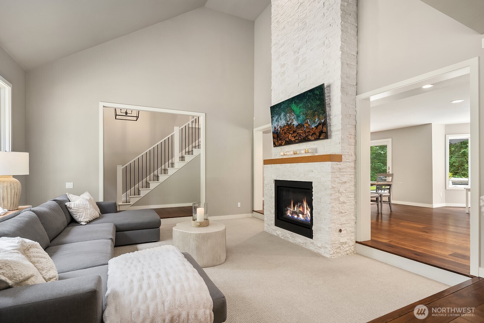 Another angle of the great room highlights the soaring two-story ceilings, elegant staircase, and fireplace, showcasing the open and airy flow between the living and dining spaces.
