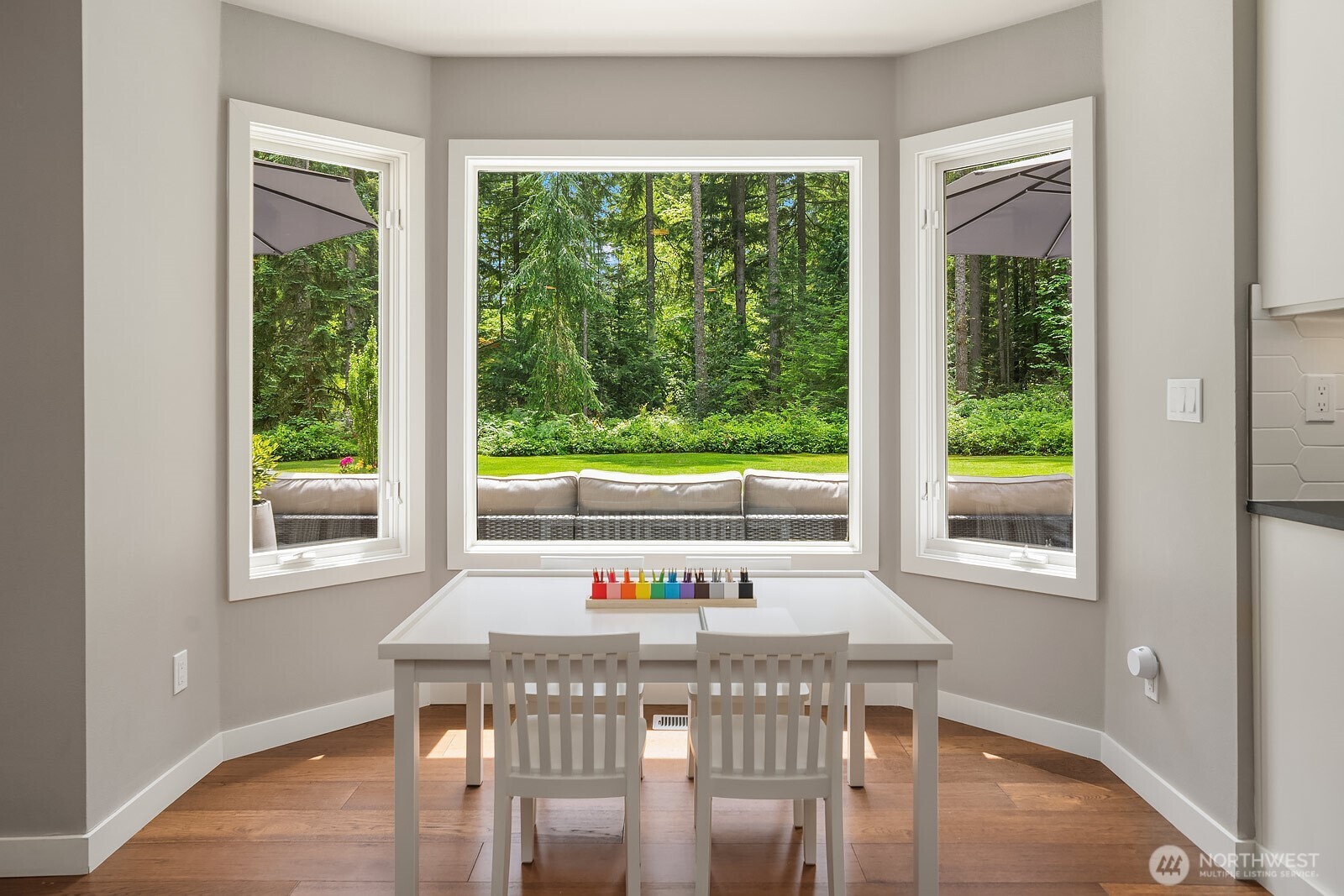 A charming breakfast nook with a wraparound bay window frames lush garden views, creating a peaceful spot to enjoy your morning coffee surrounded by the natural beauty of the private 2.22-acre setting.