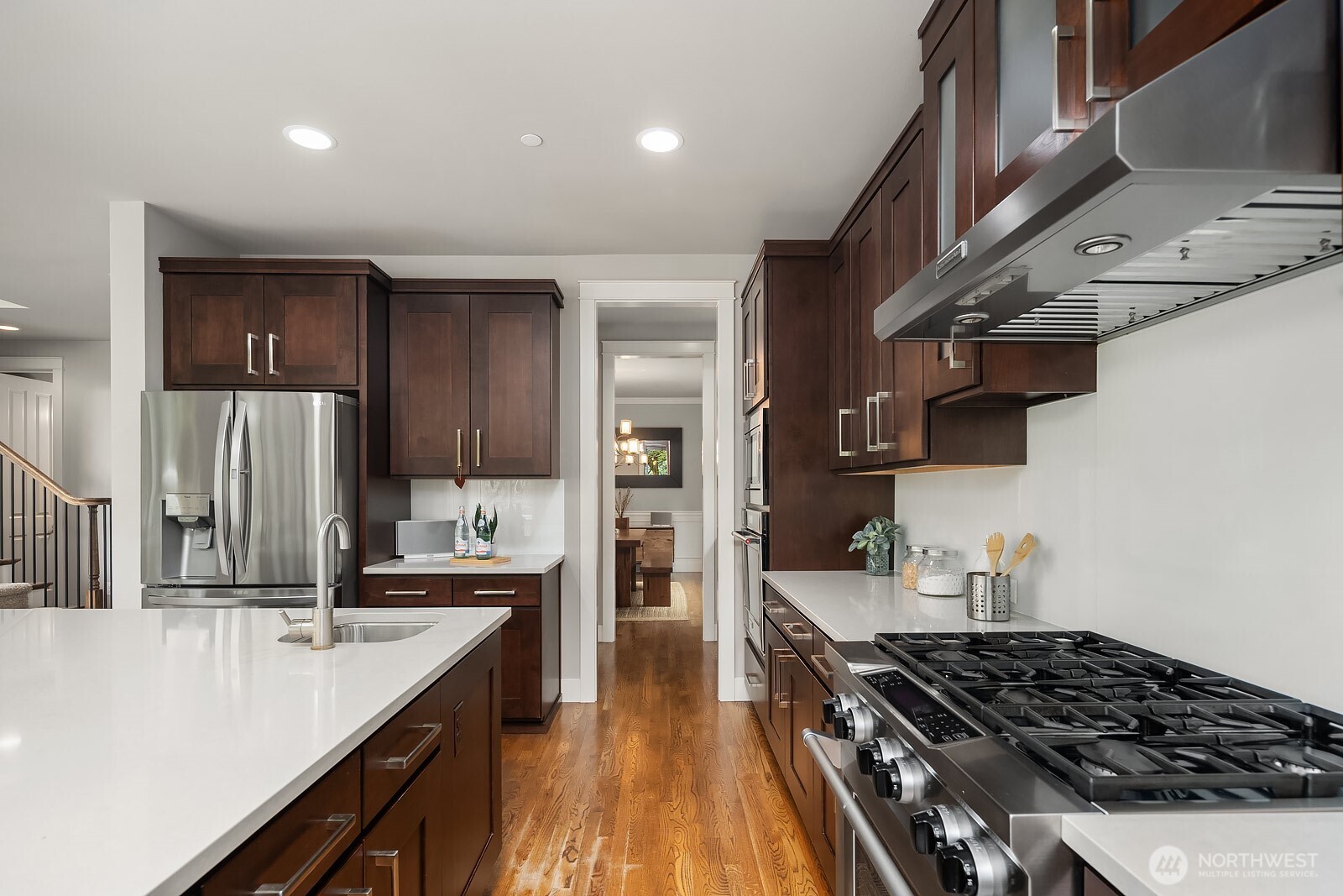 Premium stainless steel appliances, a professional-grade gas range, and rich dark cabinetry highlight the thoughtful design of this gourmet kitchen. The butler's pantry entry visible in the background speaks to the seamless flow and exceptional storage this kitchen provides.