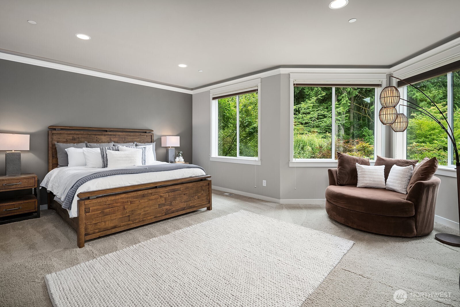 The expansive primary suite is a true sanctuary, featuring plush carpet, elegant furnishings, and a wall of windows that bathe the room in natural light while framing serene views of the lush grounds. Generous proportions and thoughtful design make this an exceptional private retreat at the end of every day.