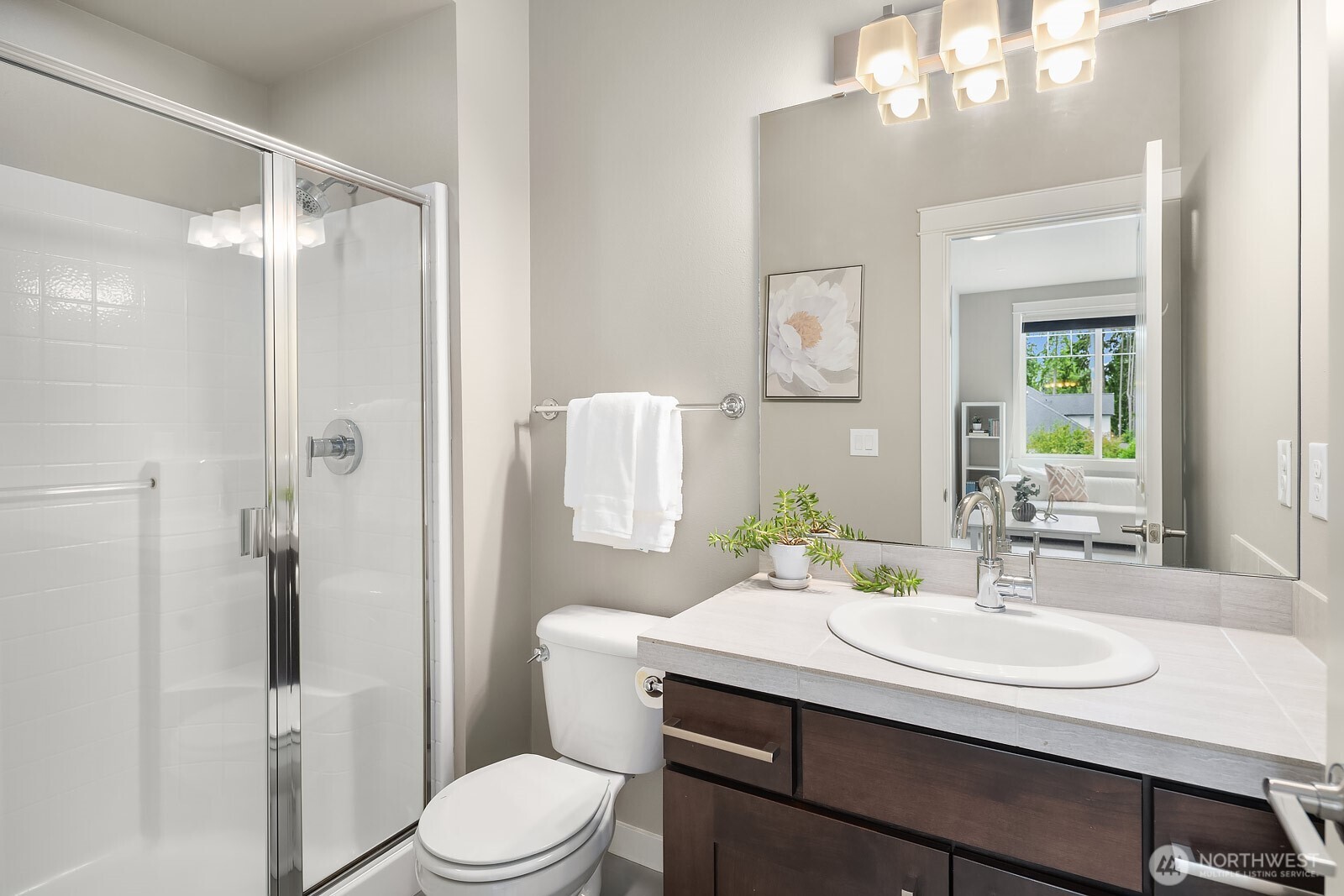 A well-appointed upper level bathroom features a walk-in shower, dark cabinetry vanity, and clean modern finishes, providing comfortable and stylish accommodations for family or guests.