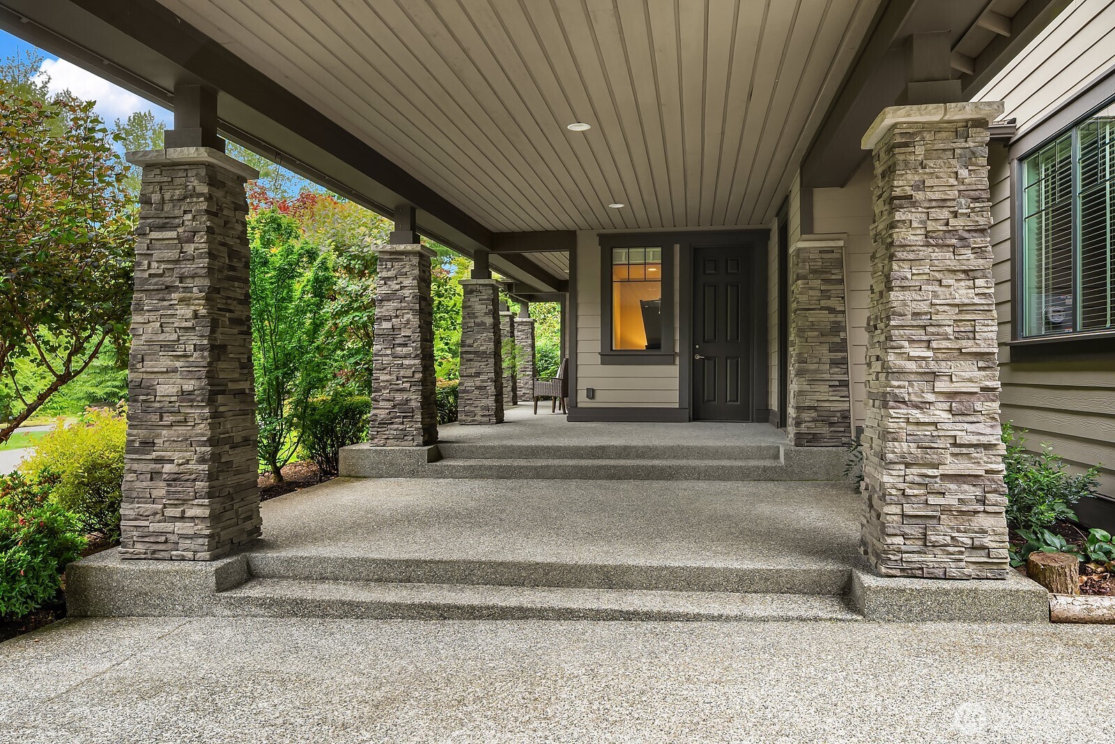 The generous covered patio entry showcases stunning stone accents, a beautifully finished ceiling, and ample space for outdoor furniture, creating an inviting transition between the home's interior and its spectacular grounds.