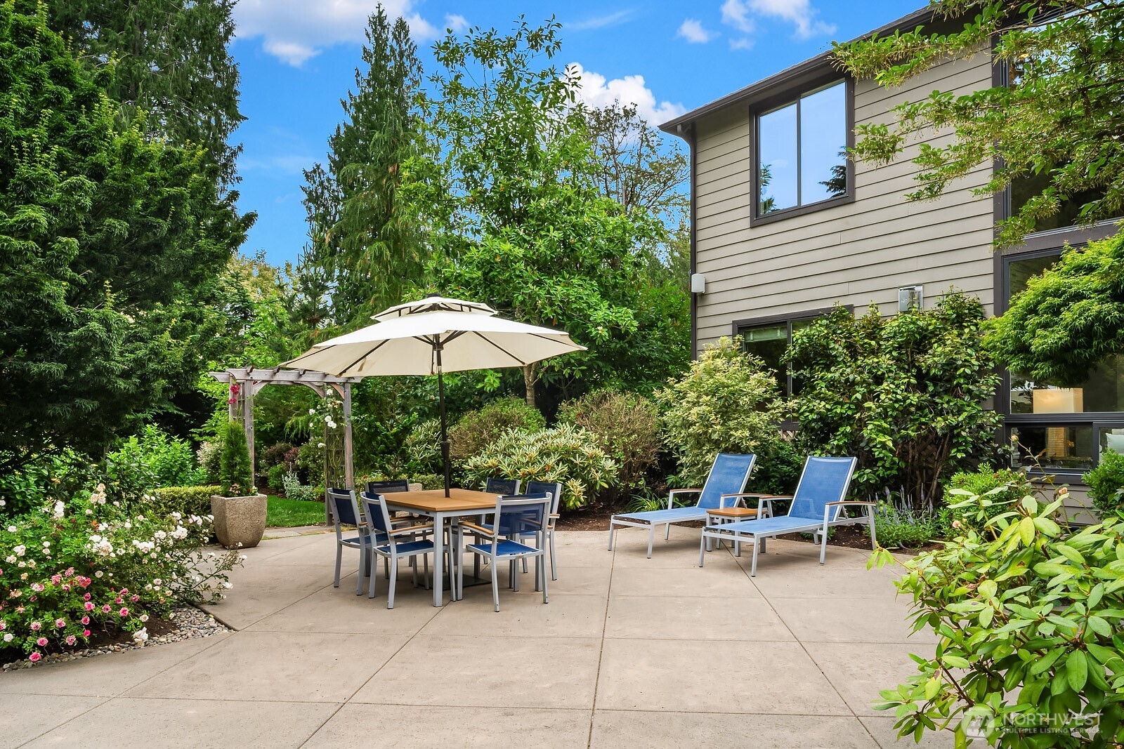 A charming outdoor dining patio is nestled among lush mature plantings and towering trees, offering a serene and private setting for al fresco entertaining just steps from the home.