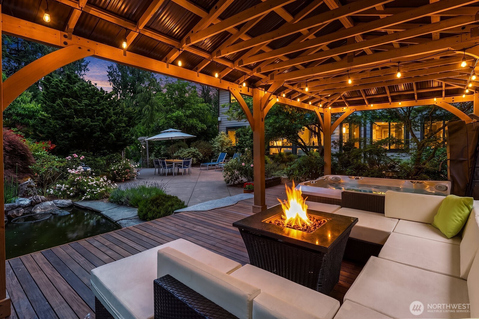 The covered outdoor living area is an entertainer's dream, featuring a stunning pergola strung with warm Edison lights, a raised gravel fire pit, and a beautifully landscaped backdrop that creates a magical ambiance day or night.