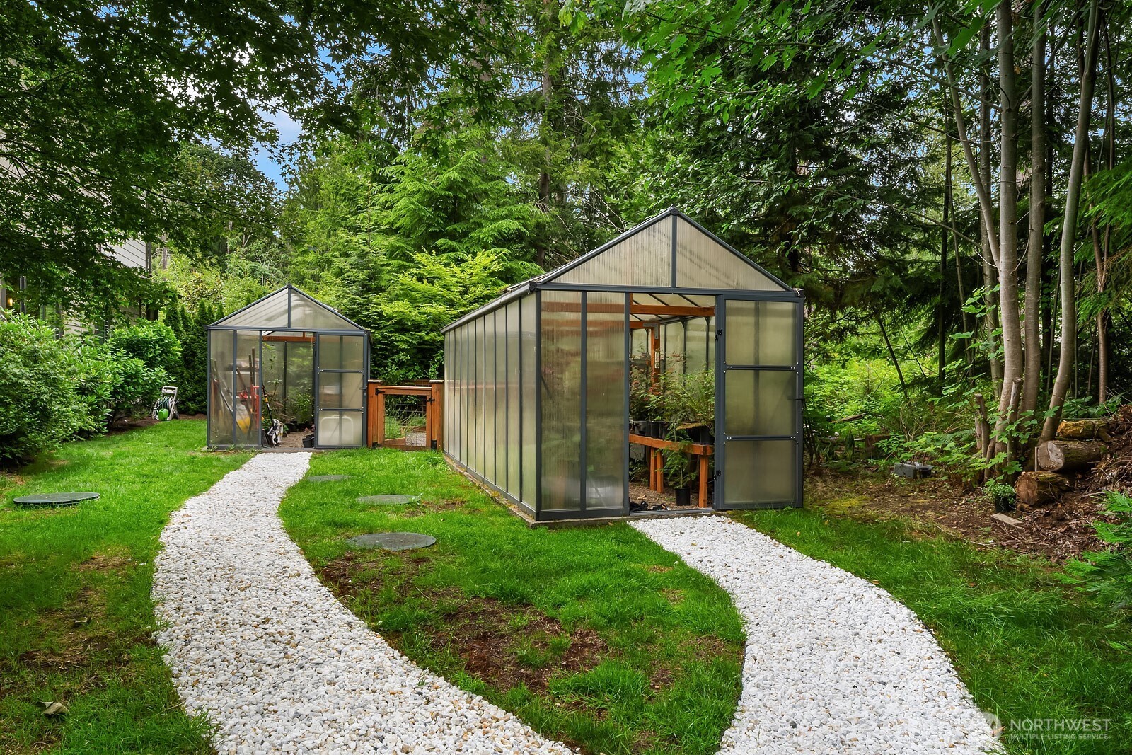 Two charming greenhouses are connected by a meandering gravel pathway, offering incredible potential for the avid gardener surrounded by the privacy and beauty of the lush, wooded grounds.