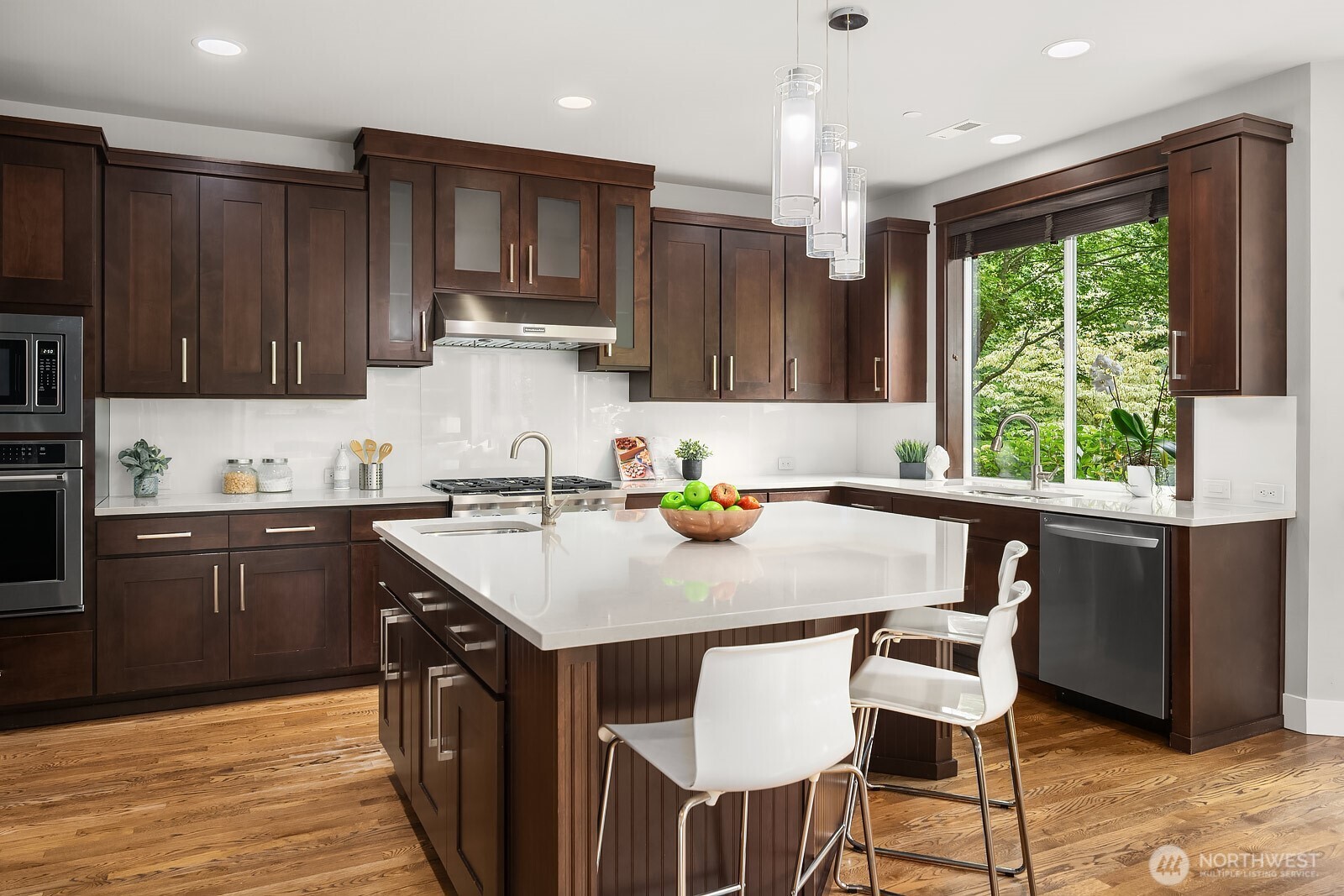 A closer look at the chef's kitchen highlights the abundant dark cabinetry, ample counter space, and high-end appliances that make this space as functional as it is beautiful. The large island with bar seating and a sun-filled window create the perfect gathering spot for family and guests alike.