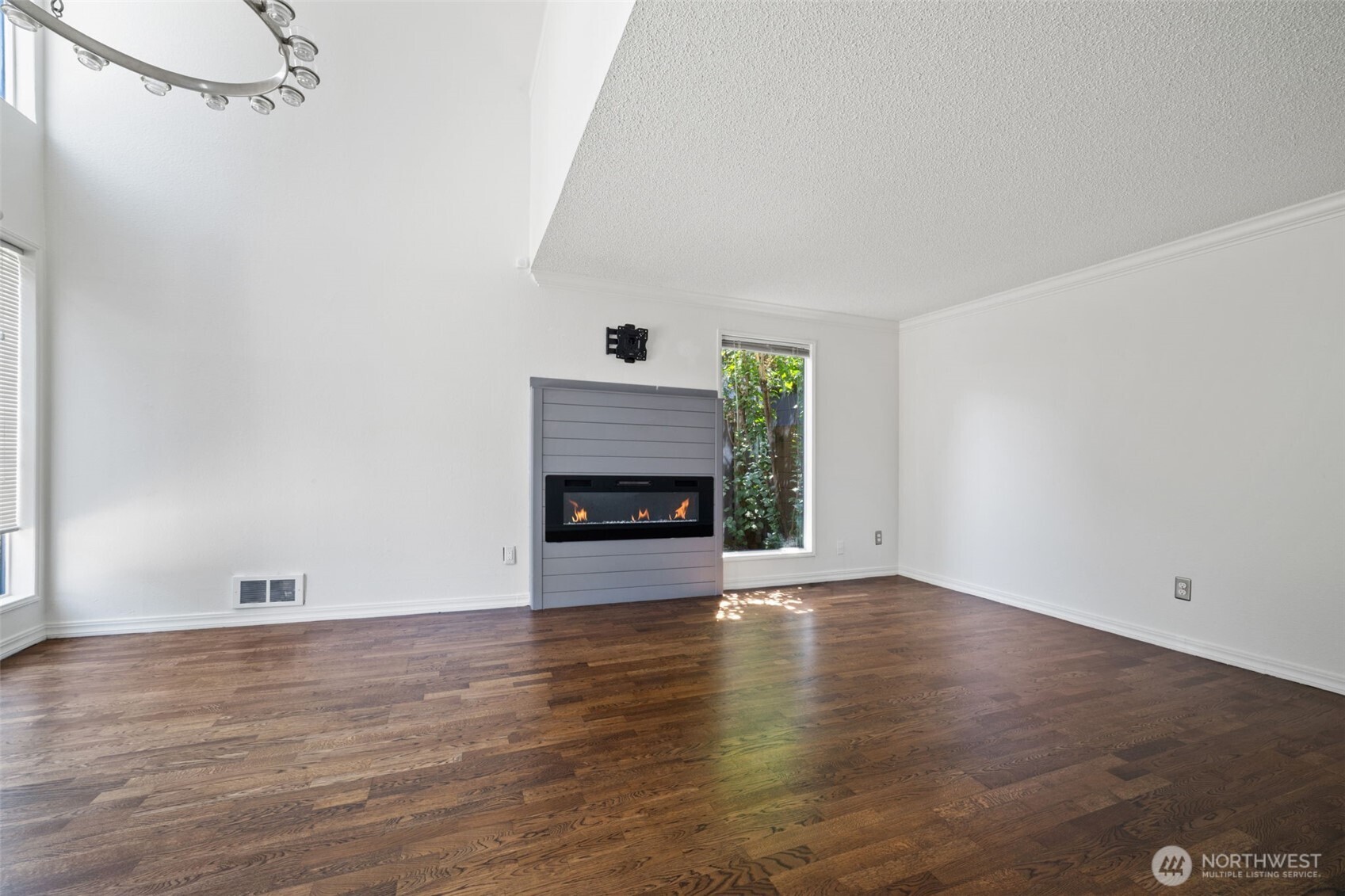 Living room with electric fireplace and vaulted ceilings open to a large fenced outdoor patio with storage shed.