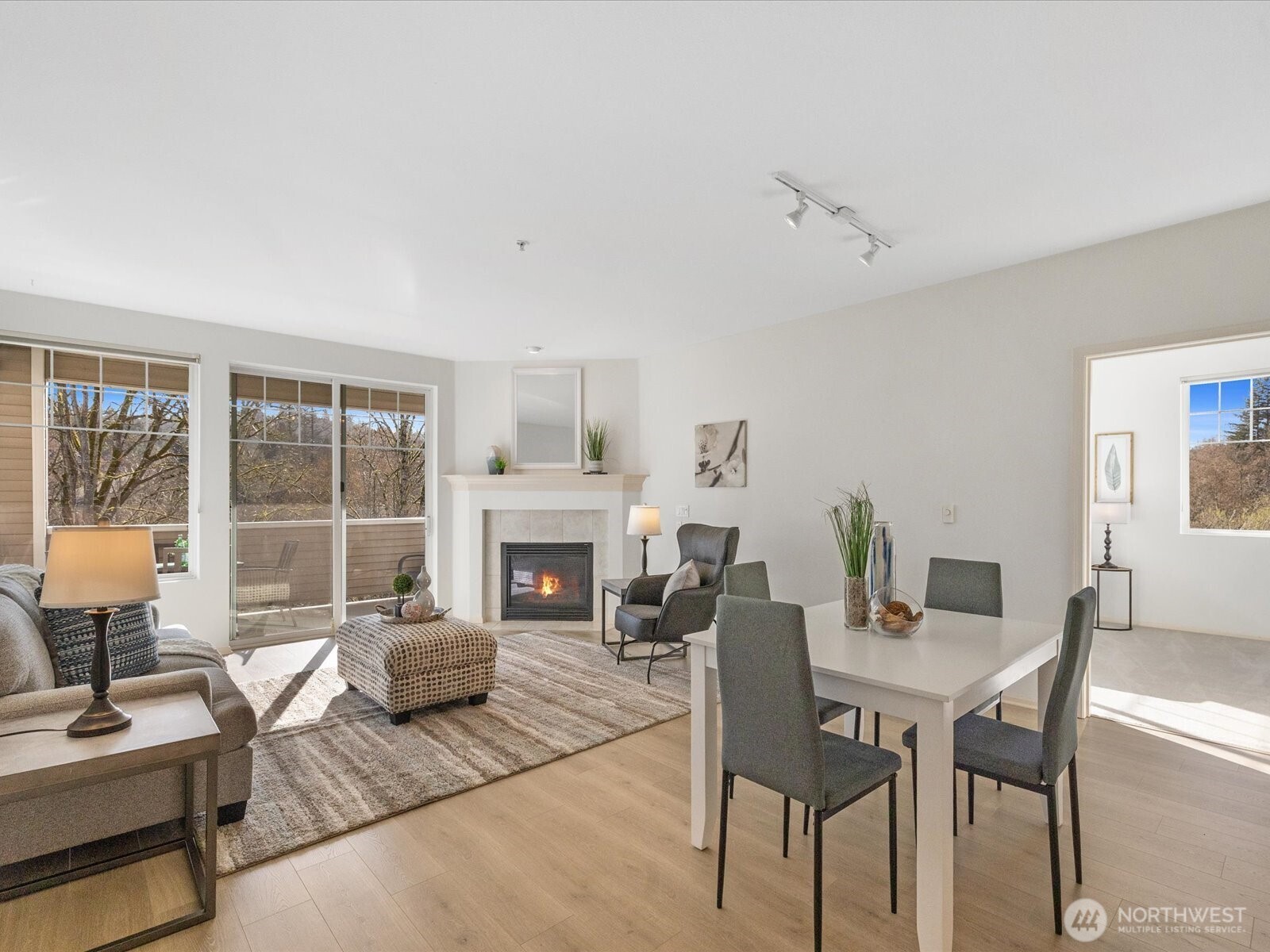 Open living and dining area with gas fireplace and sliding door access to covered deck overlooking wooded greenbelt.