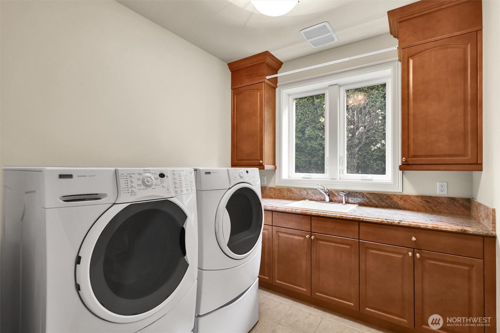 Spacious laundry room featuring granite slab countertops, a deep sink, and abundant cabinetry for exceptional storage and functionality.