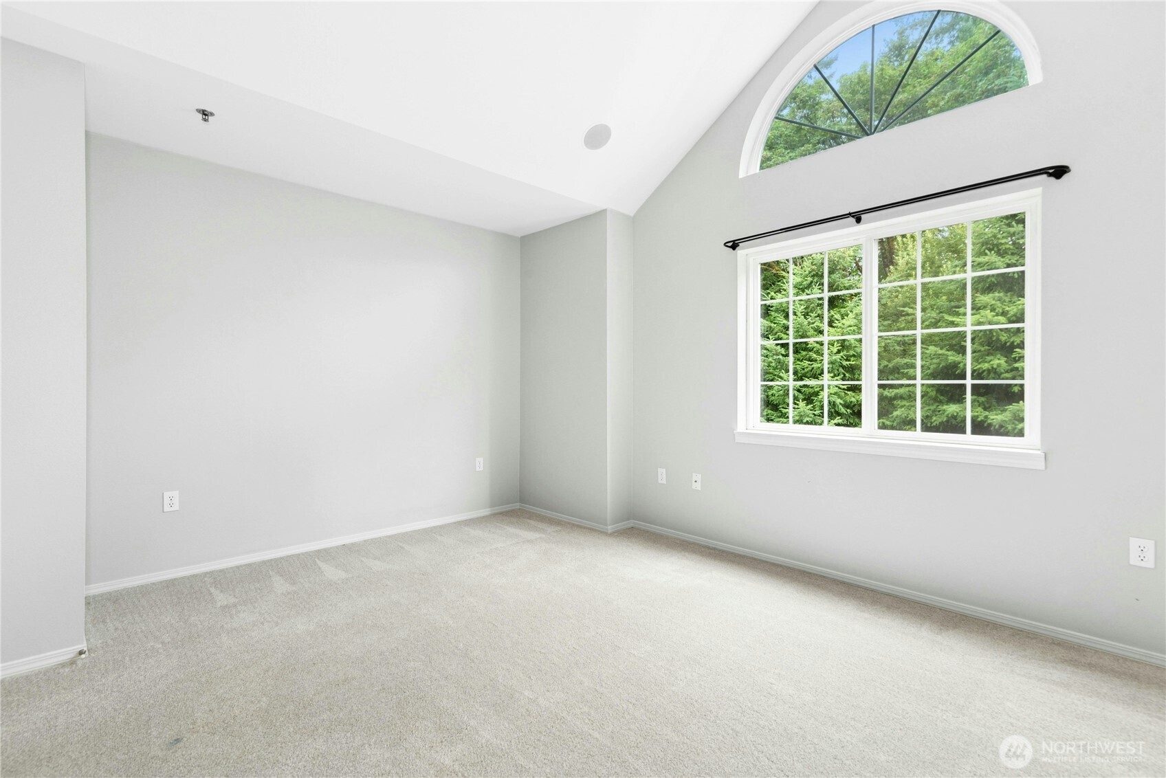 Primary bedroom with vaulted ceilings, large arched window, and abundant natural light.