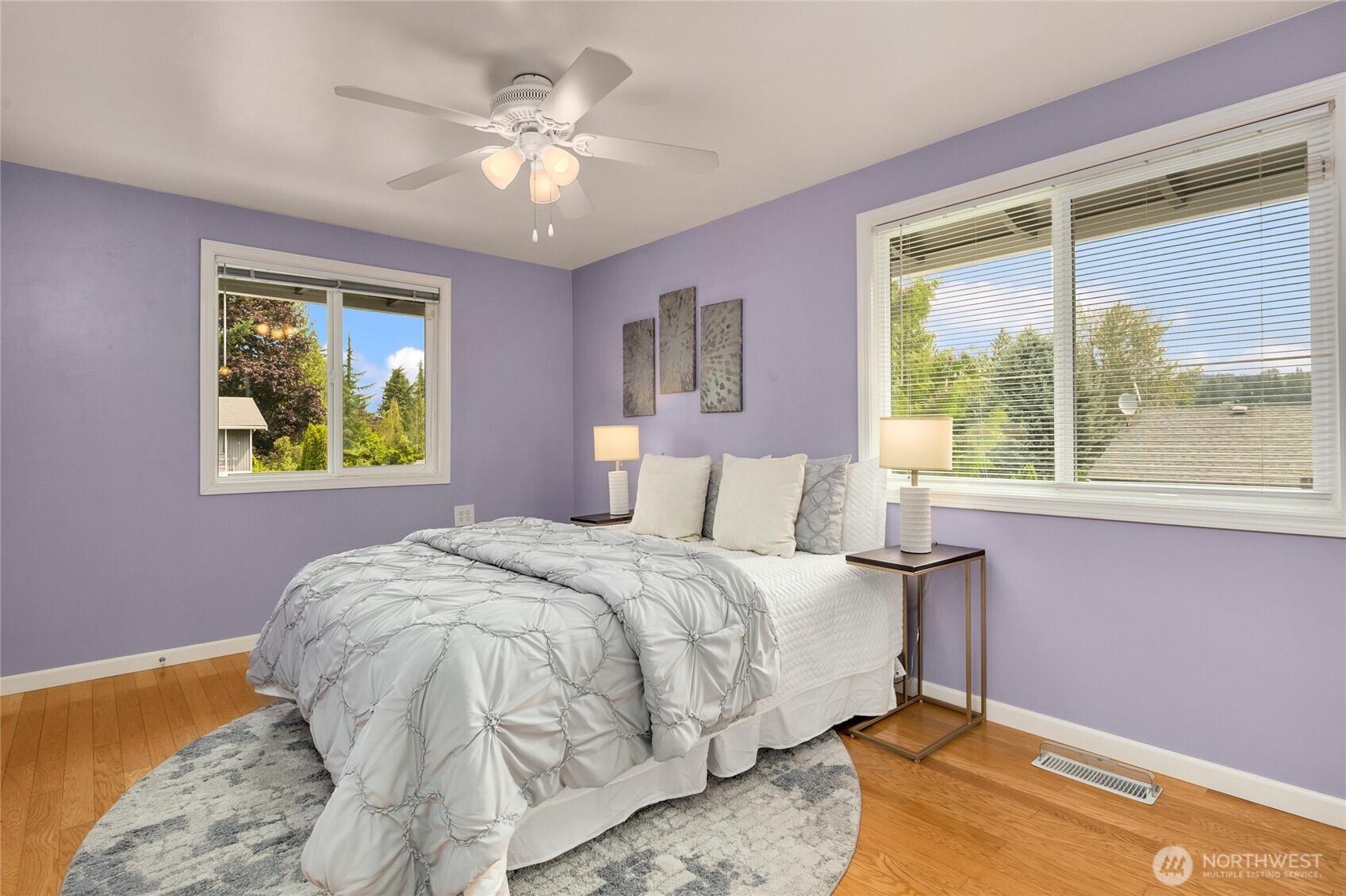 Primary bedroom with hardwood floors and ceiling fan. The en-suite bathroom is to the left.