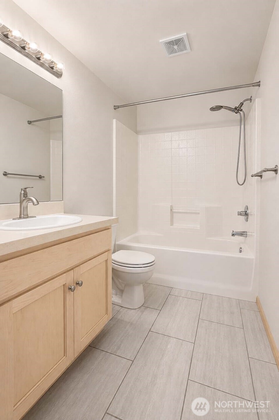 Main bath. Tile floor. Shaker-style paneled vanity cabinet with Formica®-style countertop. Newer vanity sink newer brushed nickel faucet. Vanity mirror with Chrome backed globe vanity lights.  Bathtub with faux-tile shower surround, brushed nickel rain shower wand. American Standard® watercloset.
