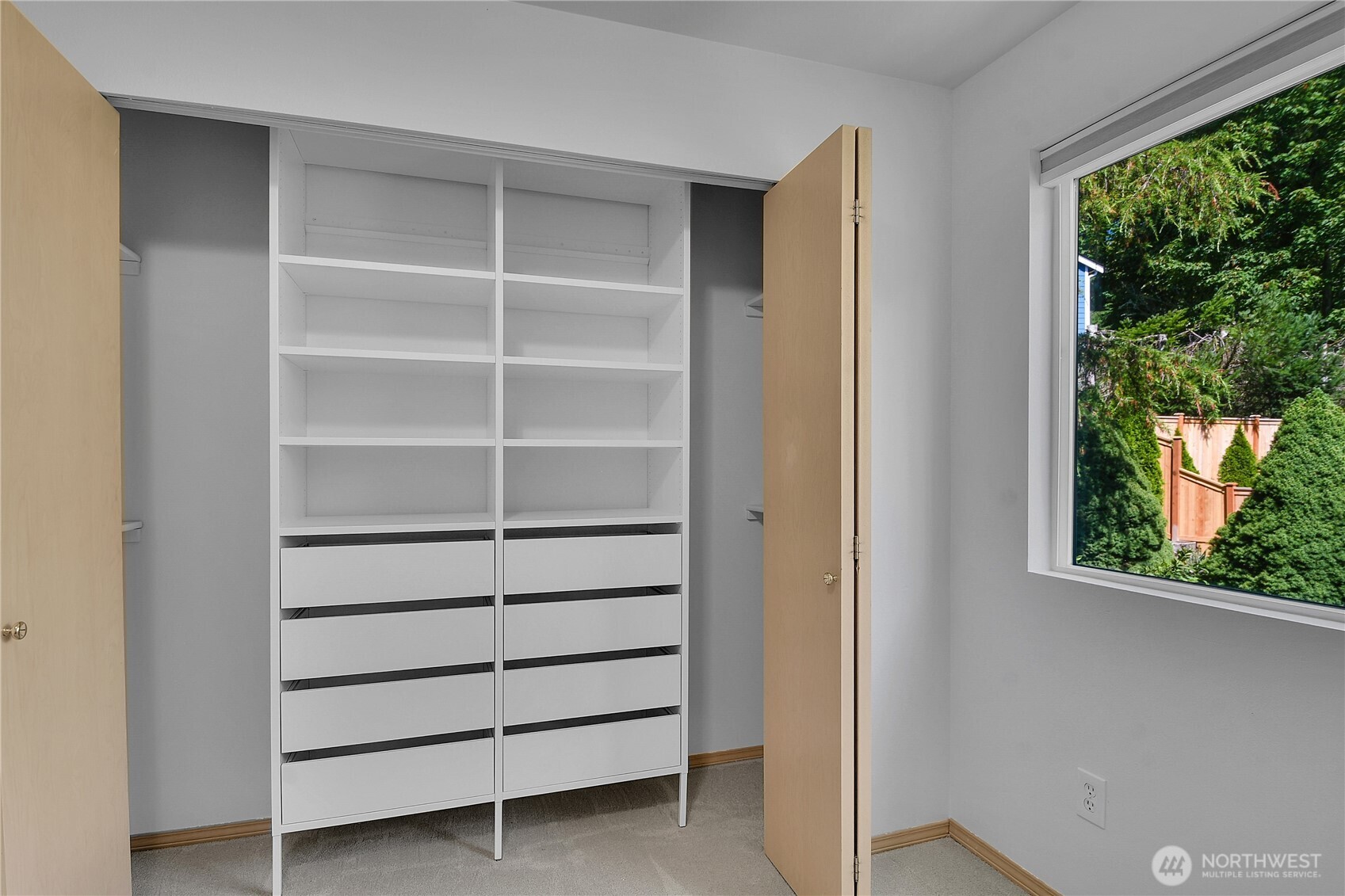 Northeast bedroom. Neutral carpet. Closet with paneled bi-fold doors. Window with screen and pulldown shade. View of Arboretum landscape.
