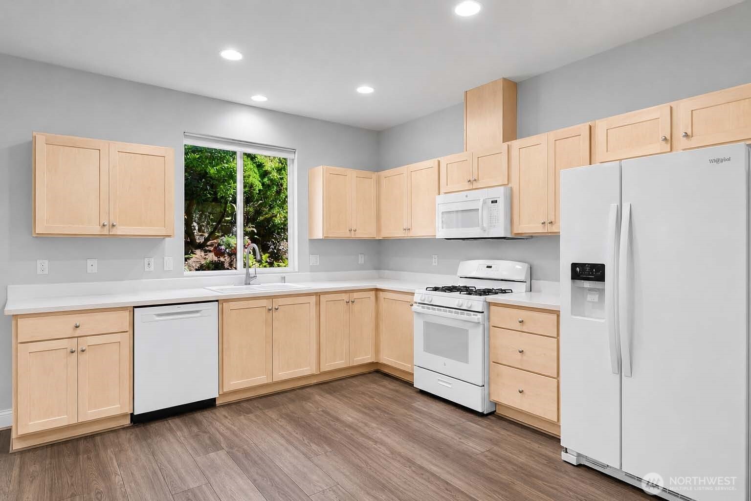 Great Room with kitchen, living and dining areas. Kitchen with newer appliances. GE® dishwasher (2025). Window at sink with screen and pulldown shade. Newer Kohler® double sink. Newer disposal (2021). Newer brushed nickel pull-down spray faucet. Formica®-style countertops. GE® gas range and gas oven (2024) with newer built-in GE® microwave oven (2021) above. Whirlpool® side-by-side refrigerator-freezer (2025) with handy exterior ice and water dispenser.