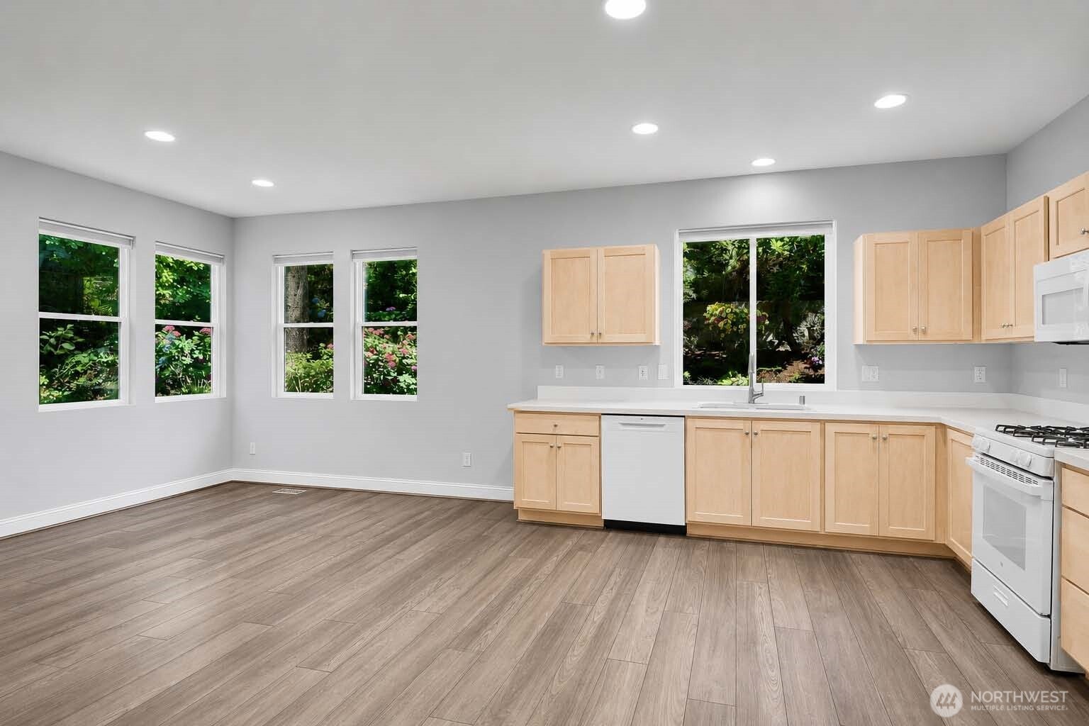 Great Room with kitchen, Living and dining Areas. Kitchen with newer appliances. Four corner windows. Premium Plank “Dora Walnut” floor. Shaker-style paneled cabinets in kitchen area. GE® dishwasher. Window at sink with screen and pulldown shade. Kohler® double sink with disposal. Formica®-style countertops. GE® gas range and gas oven with built-in GE® microwave oven above. Whirlpool® side-by-side refrigerator-freezer with handy exterior ice and water dispenser.