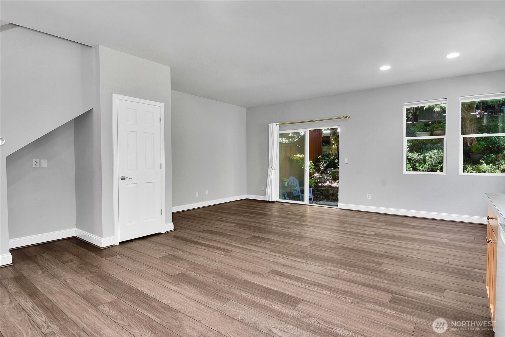 Great Room with kitchen, living and dining areas. Premium Plank “Dora Walnut” floor. Flex-nook alcove. Walk-in pantry with shelving. West wall of living area ideal for Big-Screen TV. Sliding glass door with screen door to aggregate and flagstone patio with privacy fence. Arboretum-style landscaping.