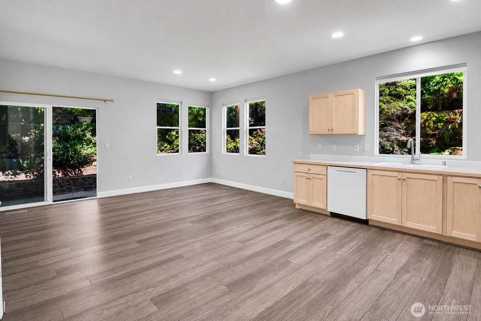 Great Room with kitchen, living and dining areas. Premium Plank “Dora Walnut” floor. Four corner windows. Sliding glass door with screen door to aggregate and flagstone patio with privacy fence. Arboretum-style landscaping.