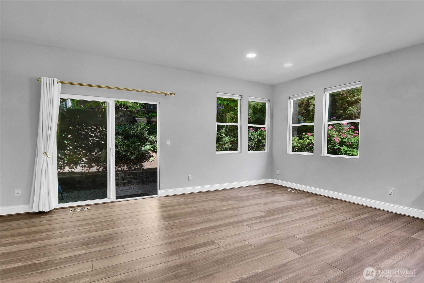 Great Room with kitchen, living and dining areas. Premium Plank “Dora Walnut” floor. Four corner windows. Sliding glass door with screen door to aggregate and flagstone patio with privacy fence. Arboretum-style landscaping.