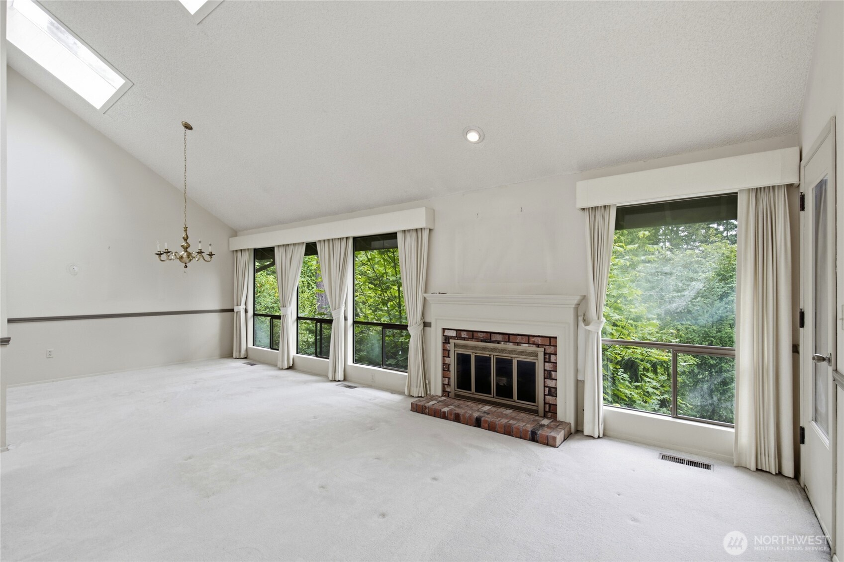 Living room with vaulted ceilings, skylight and wood burning fireplace with gas log lighter.