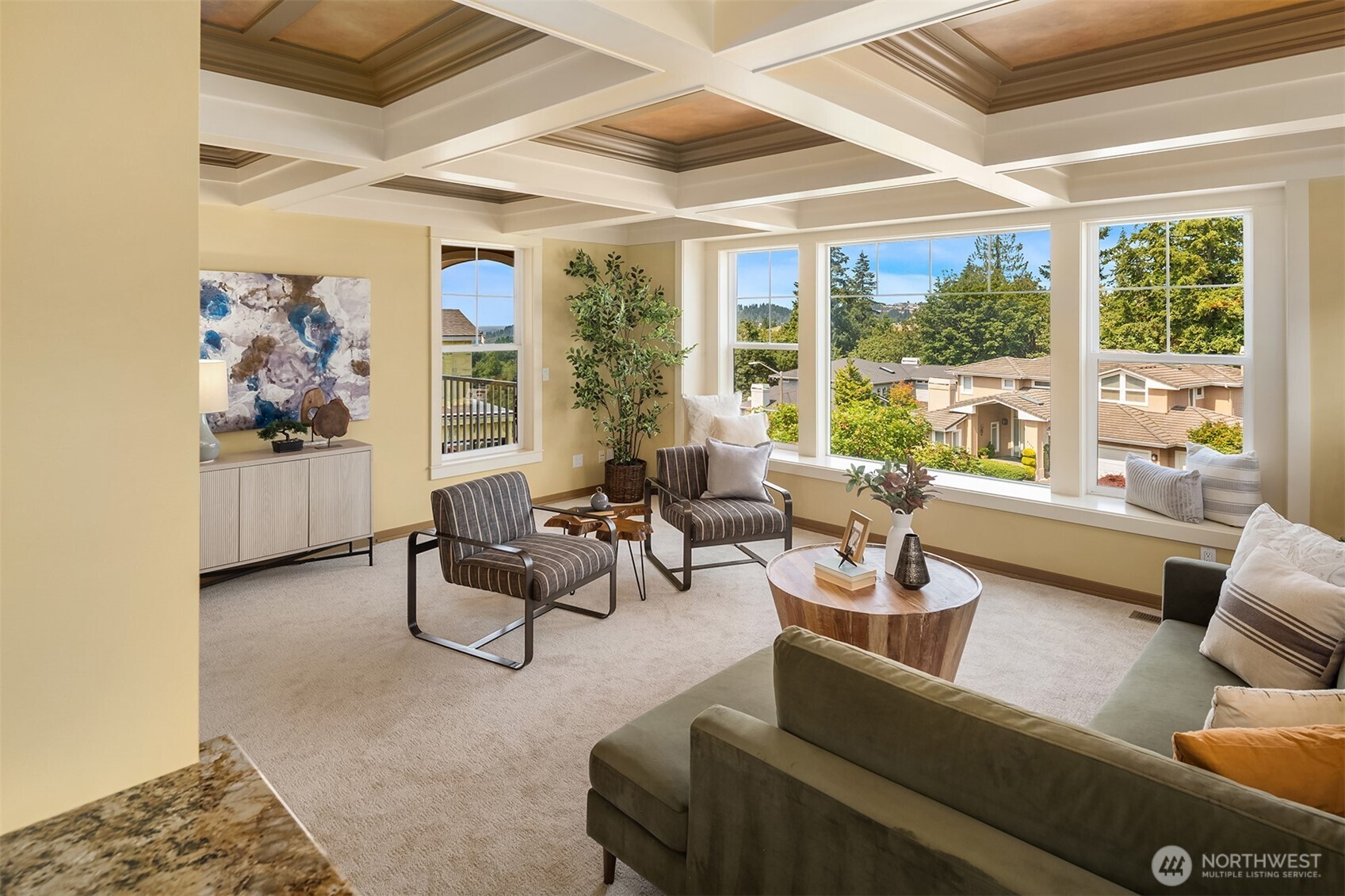 The light-filled family room is framed by oversized windows, a distinctive coffered ceiling, and peek-a-boo  views—an inviting place to relax just beyond the kitchen.