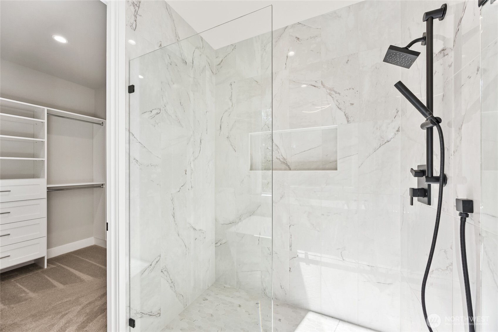 Spa inspired walk-in shower showcases floor to ceiling tile, a frameless glass shower, and designer matte black fixtures finishes.