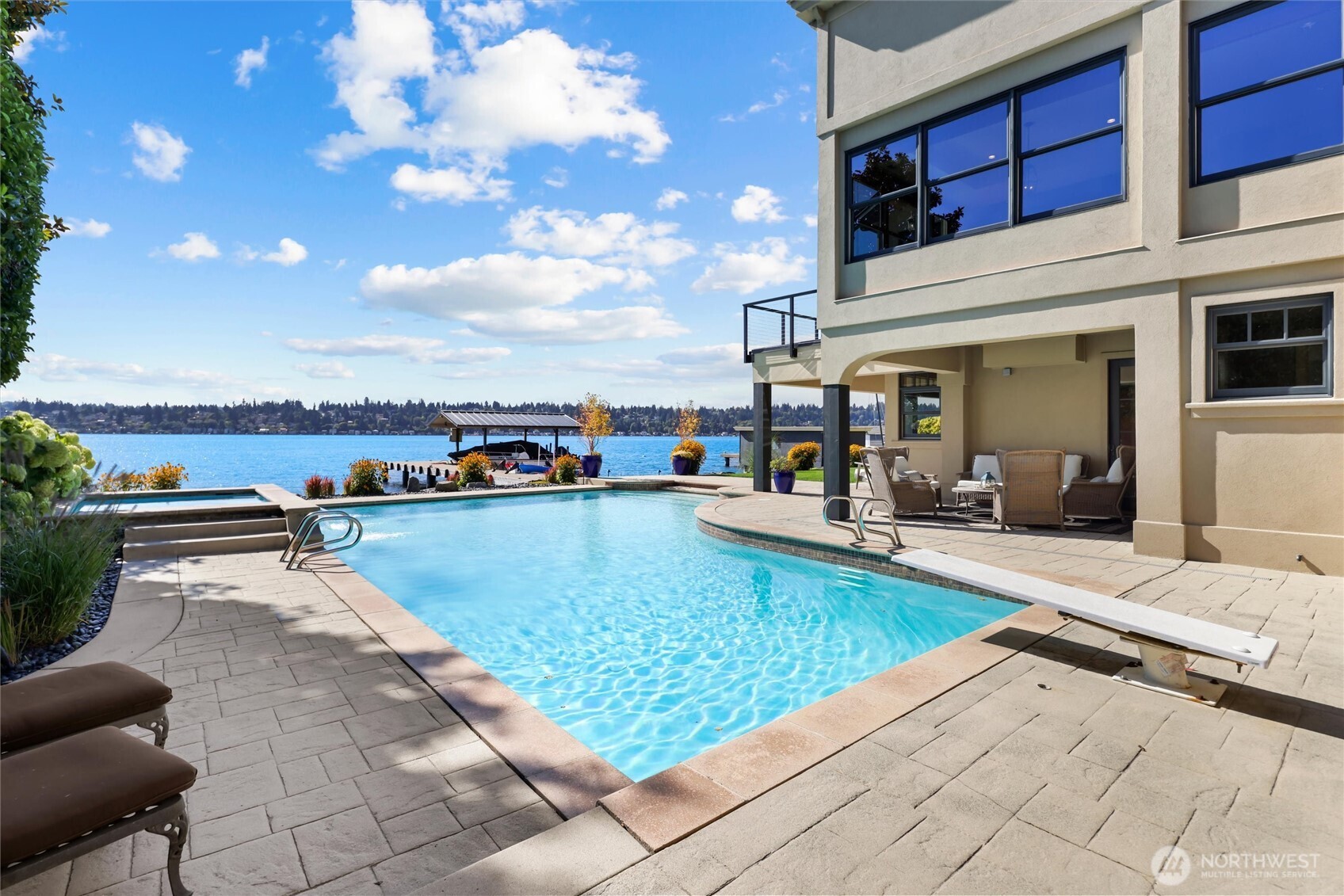 Large custom waterside in-ground pool and hot tub complete with a waterfall, diving board, and pool house storage