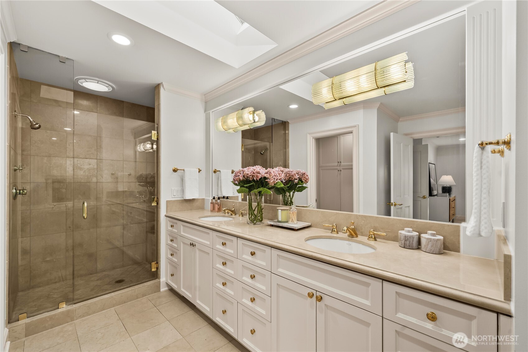 Elegant dual-sink vanity, glass-enclosed walk-in shower, abundant cabinetry, and refined finishes.
