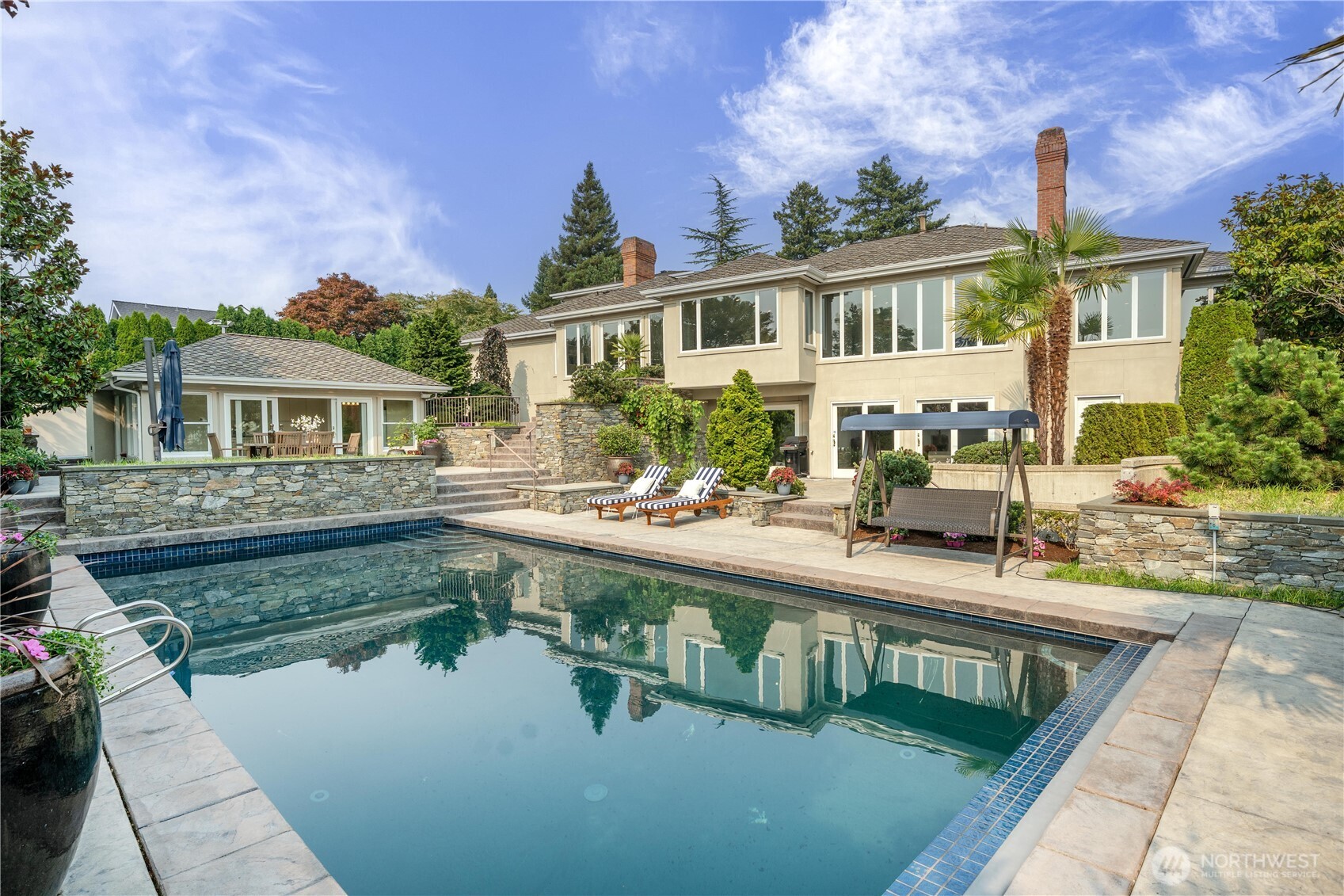 The back of the home opens to a beautifully landscaped, private outdoor oasis featuring a sparkling swimming pool, expansive stone patios, multiple lounging and entertaining areas