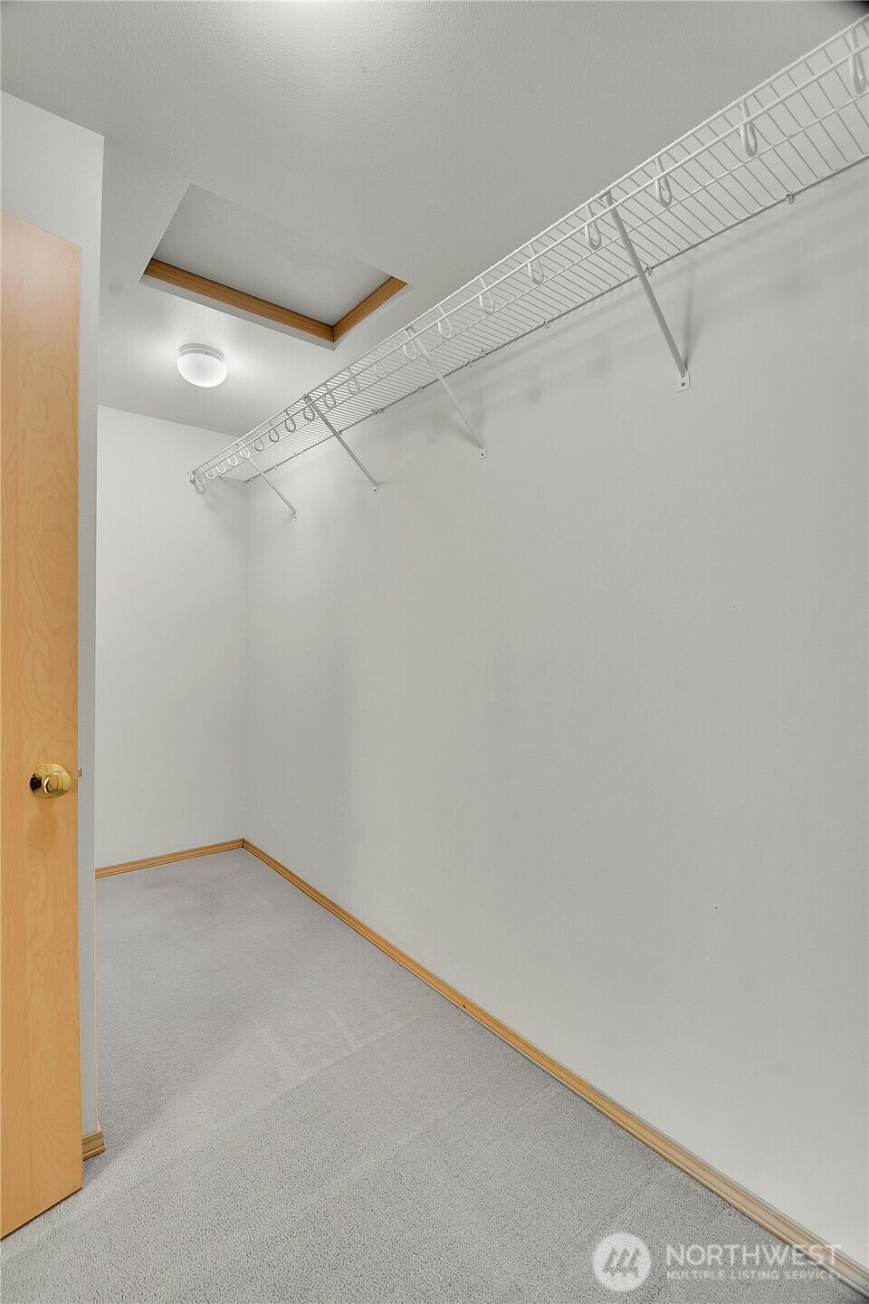 Primary walk-in closet. Powder coated ventilated wire shelf with integrated hanging rod. Neutral carpet.
